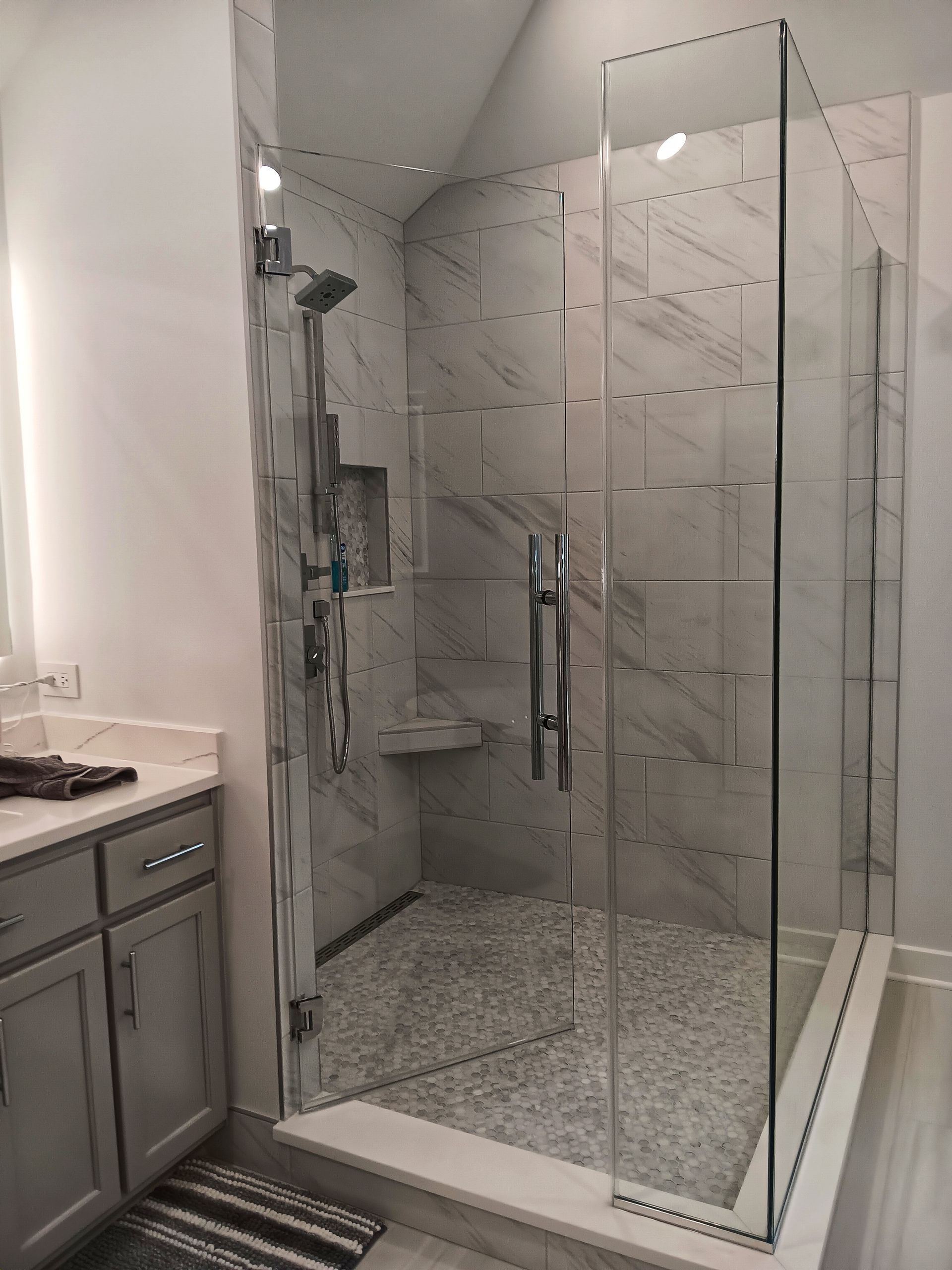 Modern glass shower enclosure with marble tile walls and pebble floor in a bathroom.