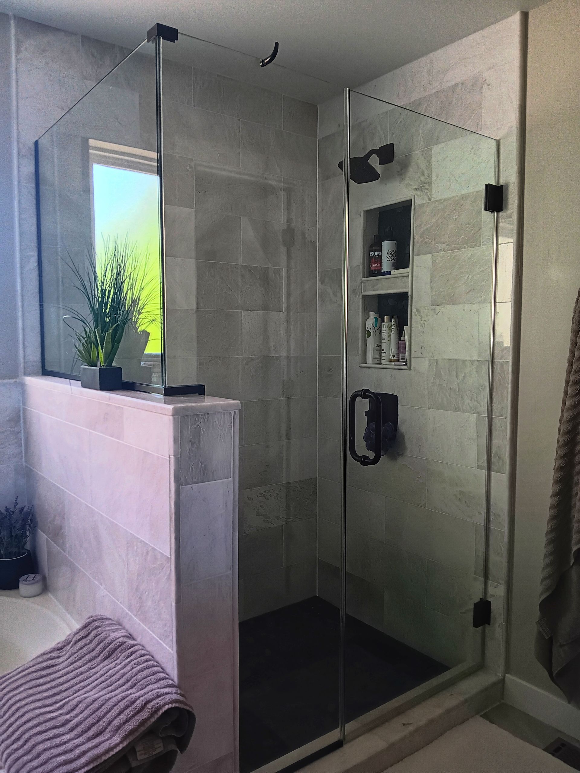 Modern glass-enclosed shower with gray tiled walls, black shower head, and a built-in shelf.