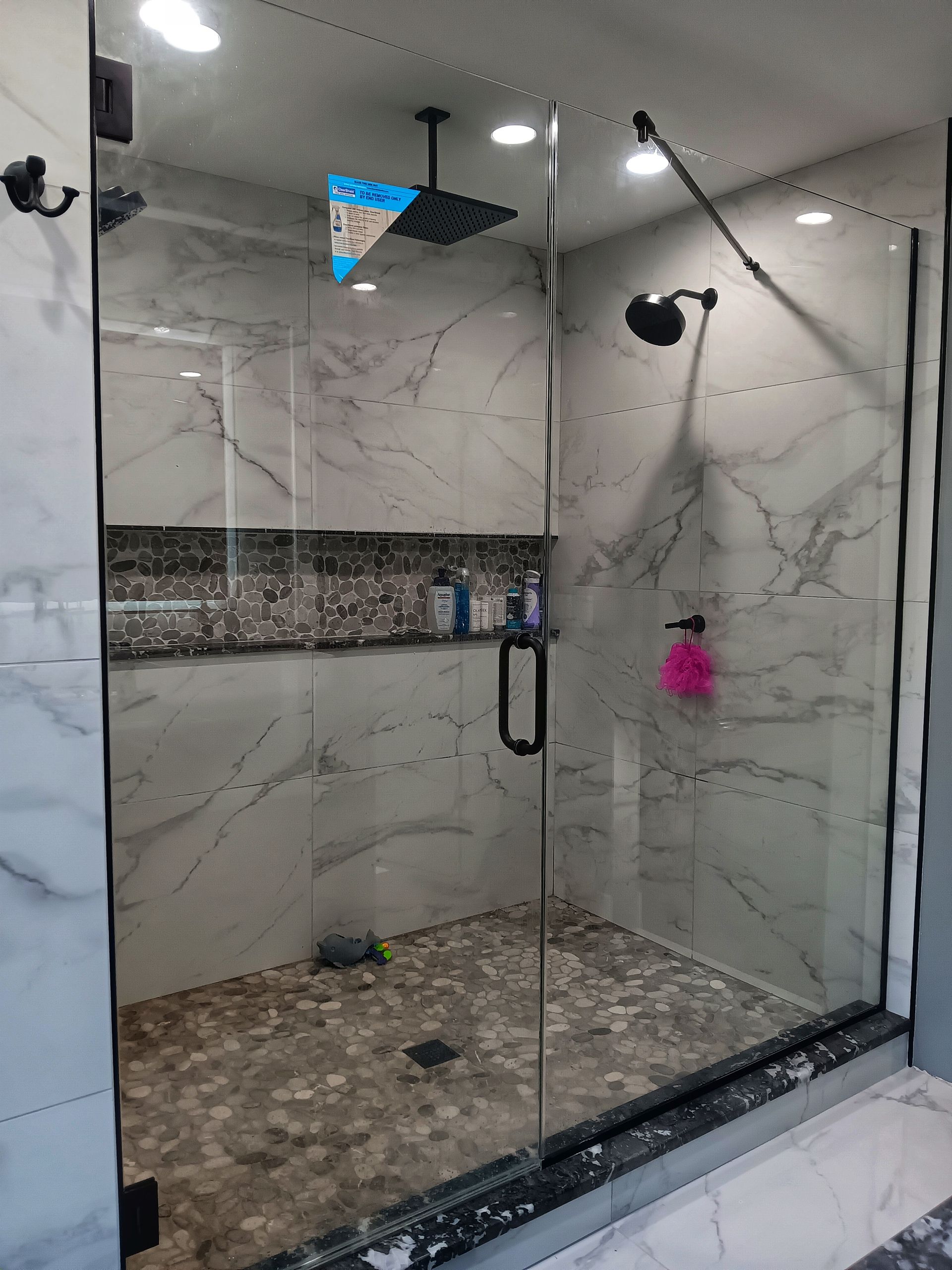 Modern glass shower with gray marble tile, pebble floor, and black fixtures.
