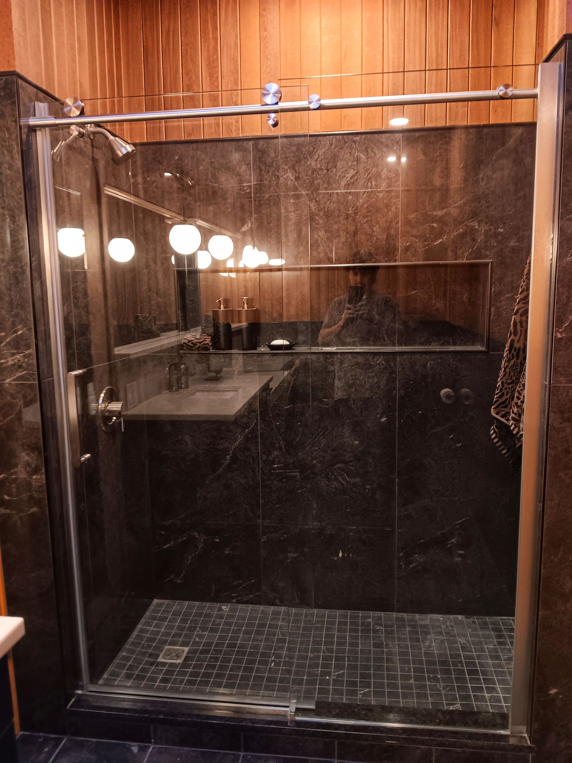 Shower with black marble tiles, a built-in shelf, and a glass door.