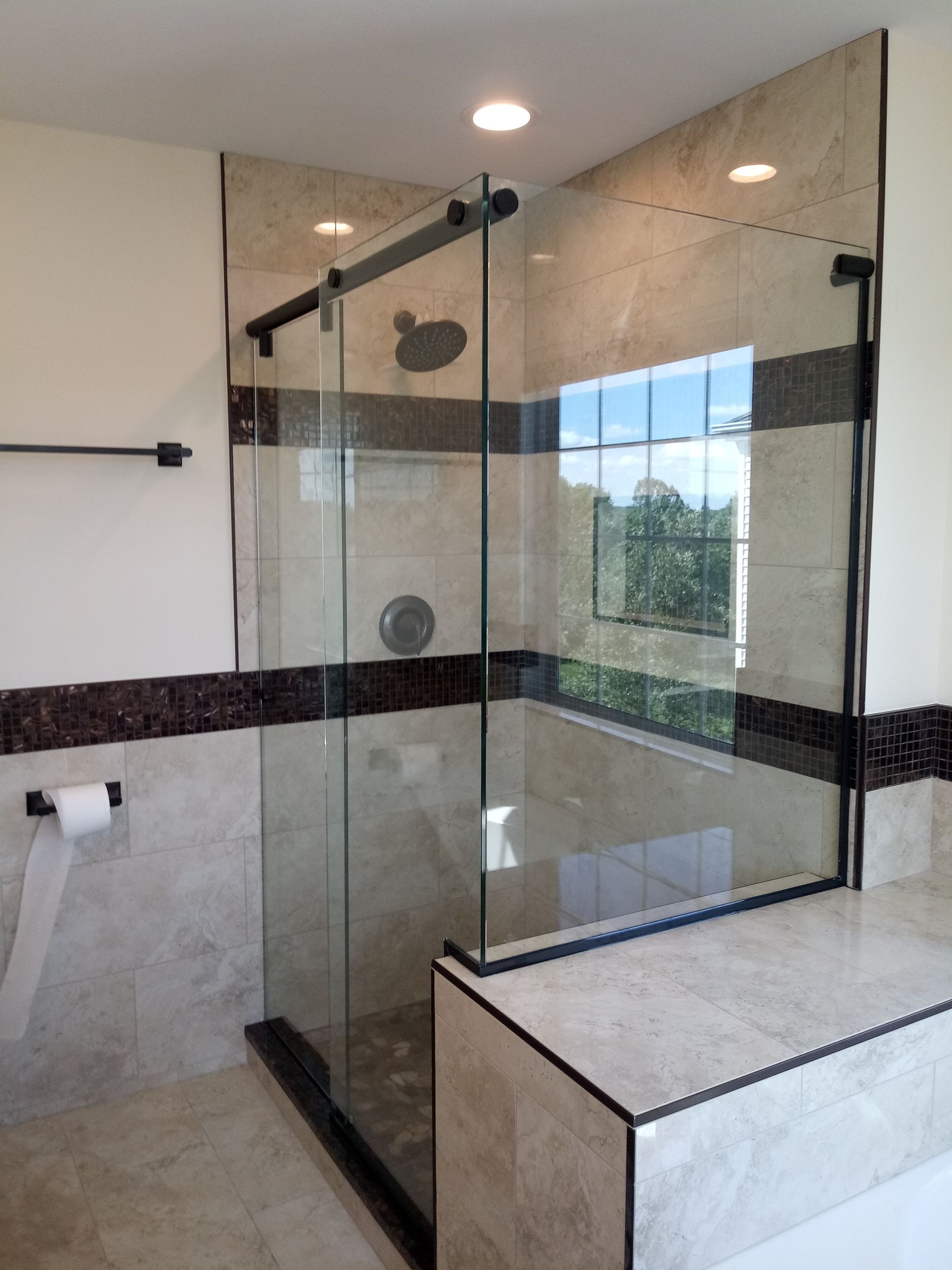 Modern shower with glass walls, black trim, and beige tile. Black showerhead and hardware.