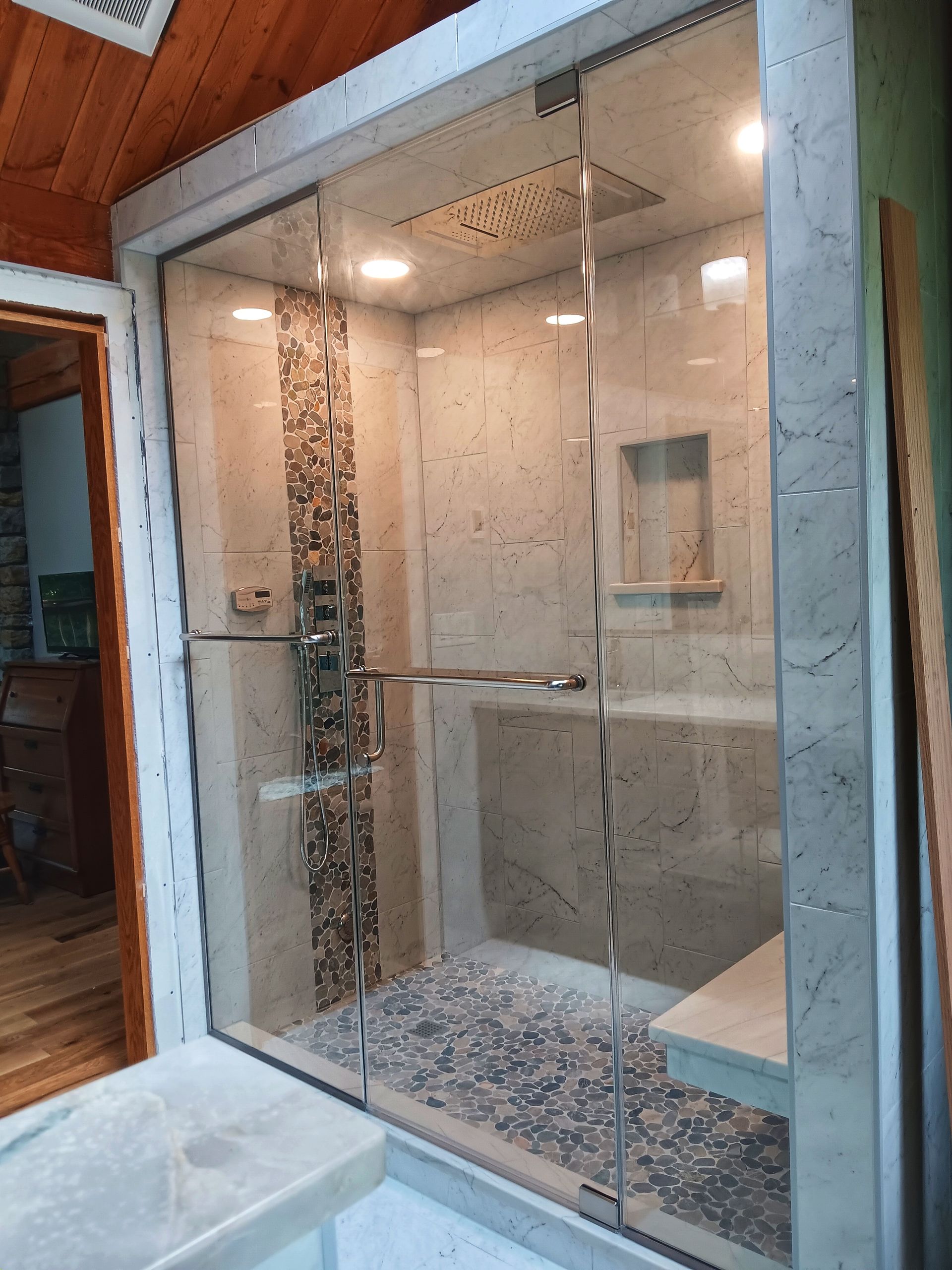 Glass shower with stone tile, pebble floor, and a bench.