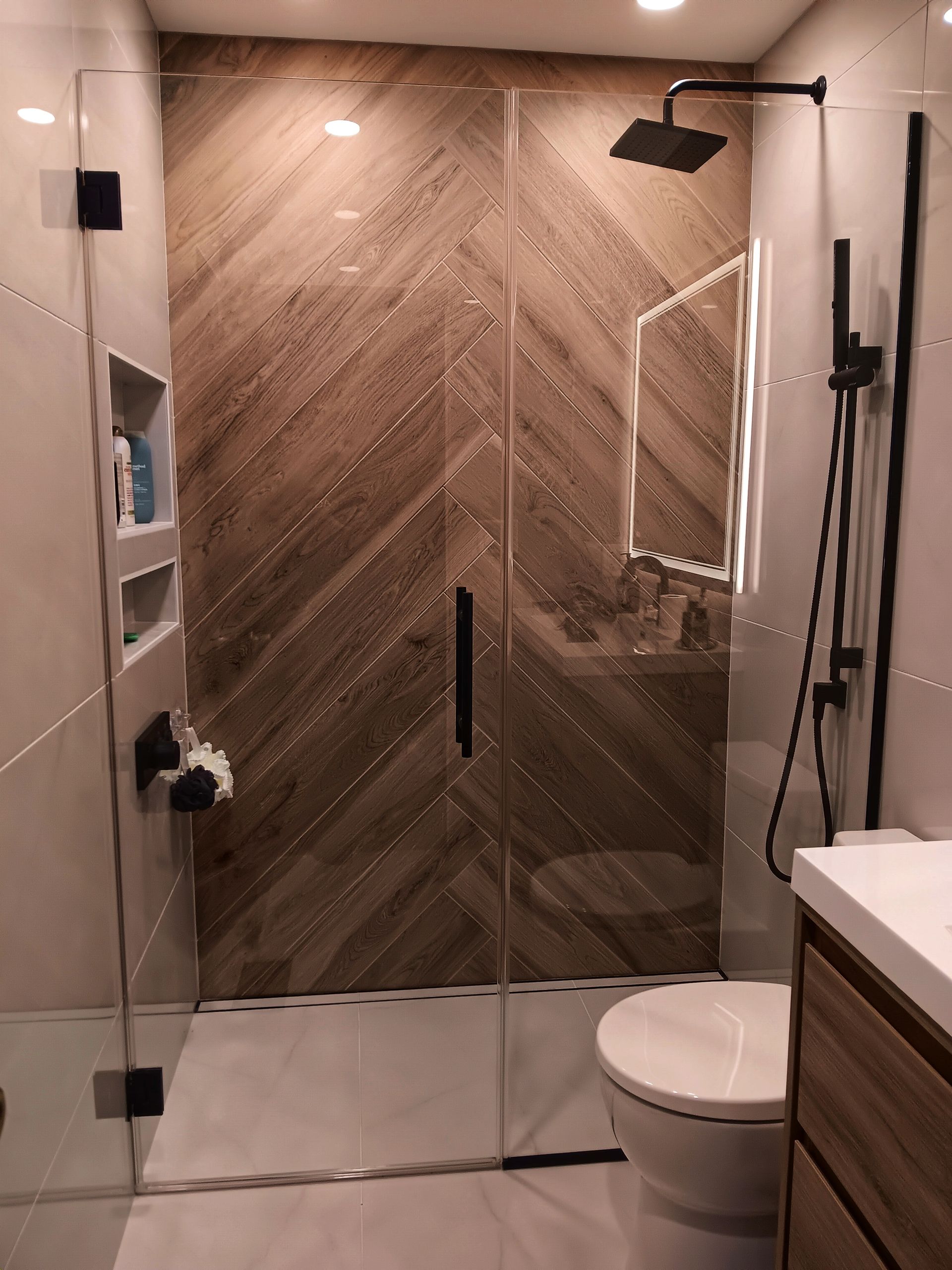 Modern shower with a brown tiled feature wall, glass doors, and black fixtures.