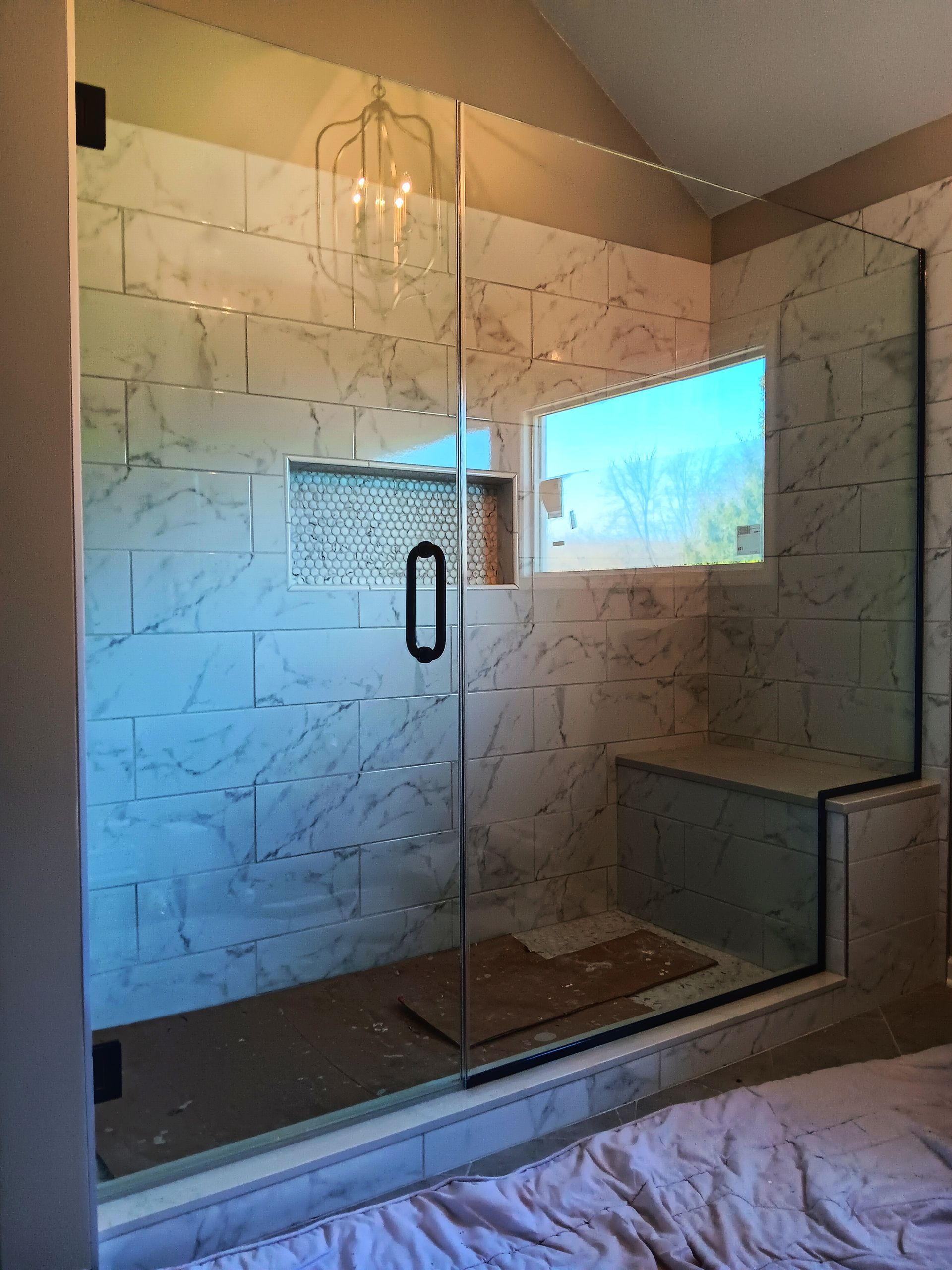 A modern, tiled shower with glass door and a small window, built-in seat, and decorative lighting.