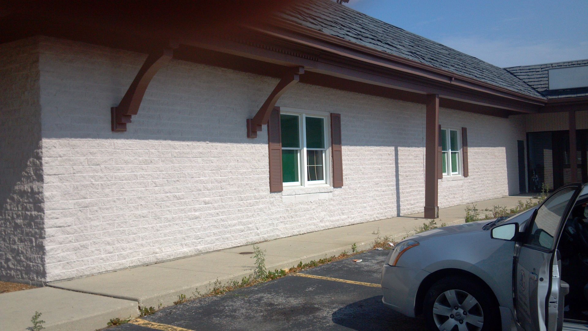 Exterior of a building with brick siding, brown trim, and a car parked in front.