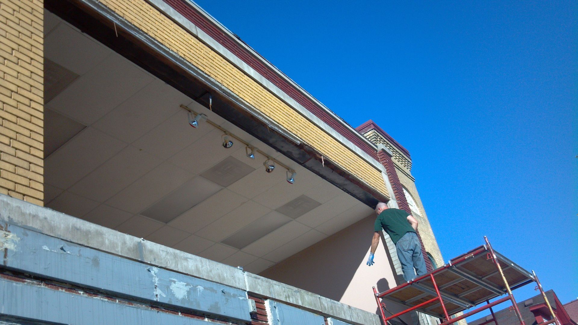 Person on a scaffold working on the exterior of a brick building under a clear blue sky.