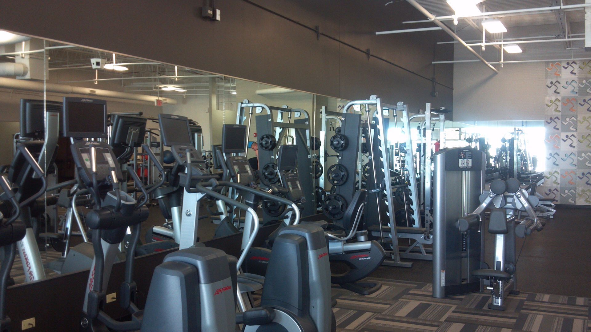 Gym interior with exercise machines, mirrors, and weights.