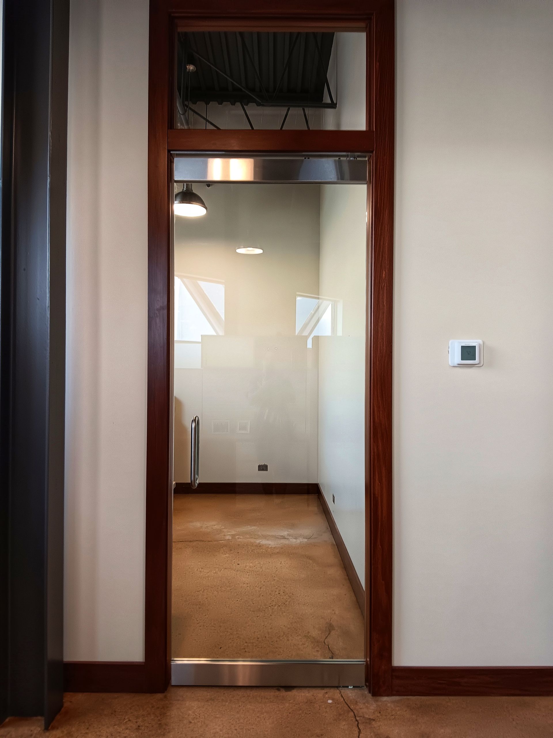 Glass-doored office with dark wood frame, light walls, and concrete floor.