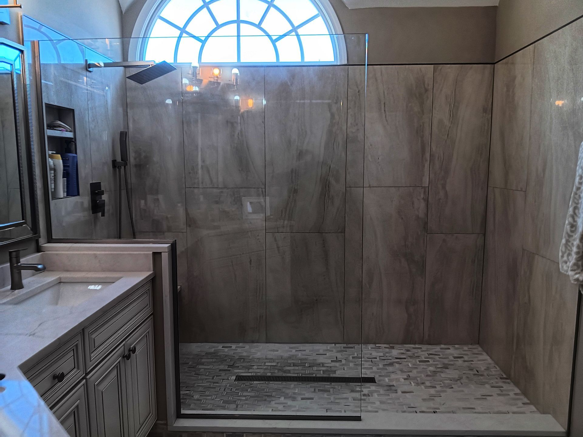 Bathroom with a walk-in shower. Beige tile walls, a glass door, and a pebble-floored shower. Vanity on the left.
