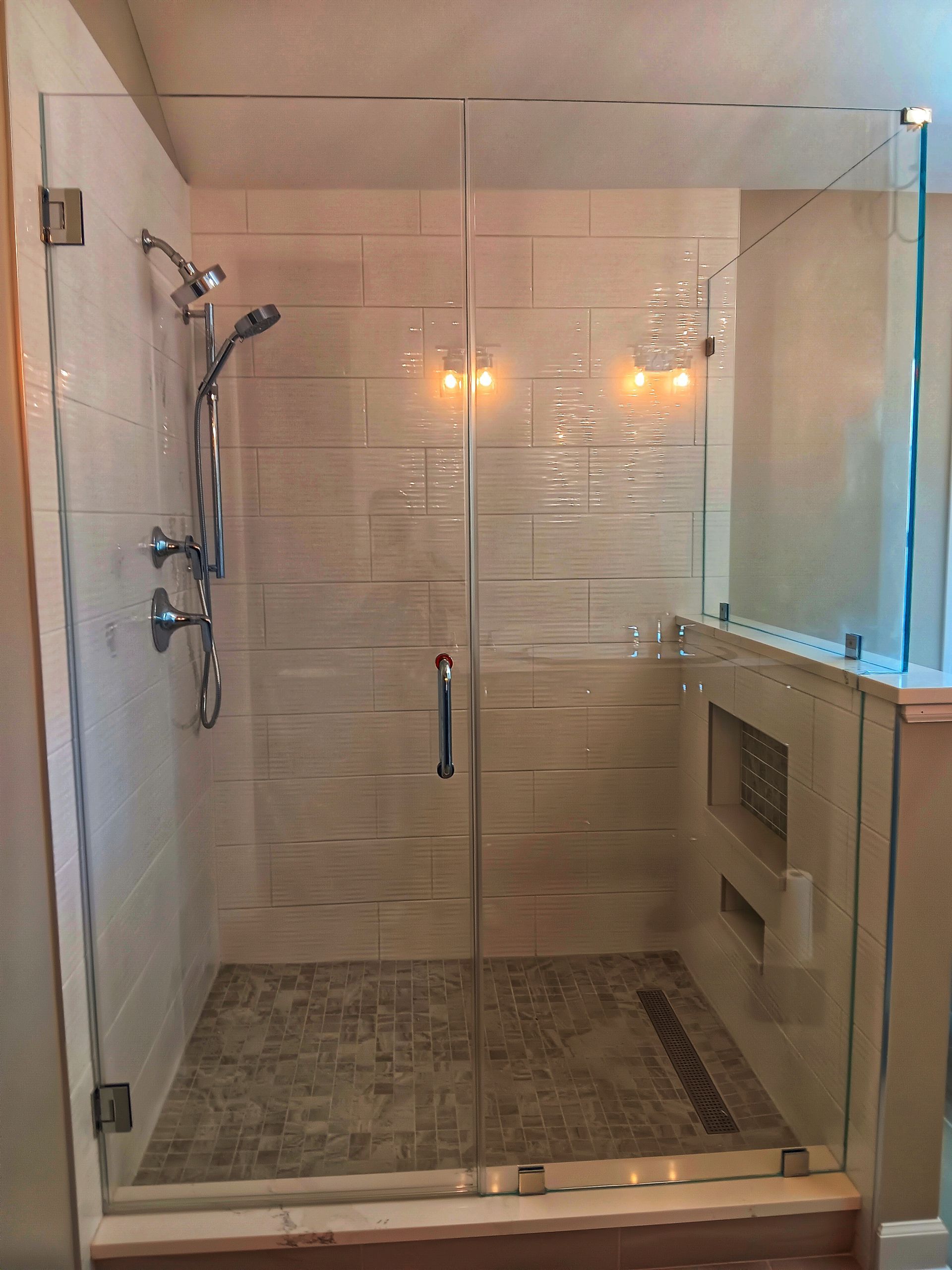 Glass-enclosed shower with beige tile walls and mosaic floor. Chrome fixtures and a handle on the glass door.