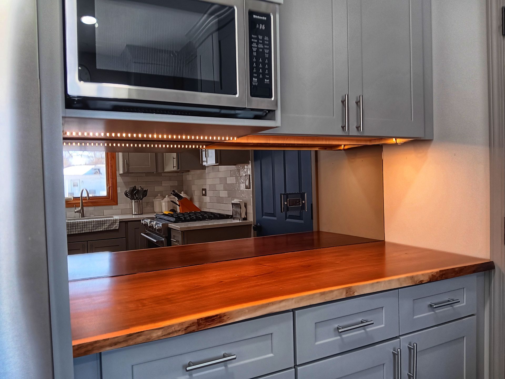 Kitchen with gray cabinets, wood countertop, microwave, and mirror backsplash reflecting the kitchen.