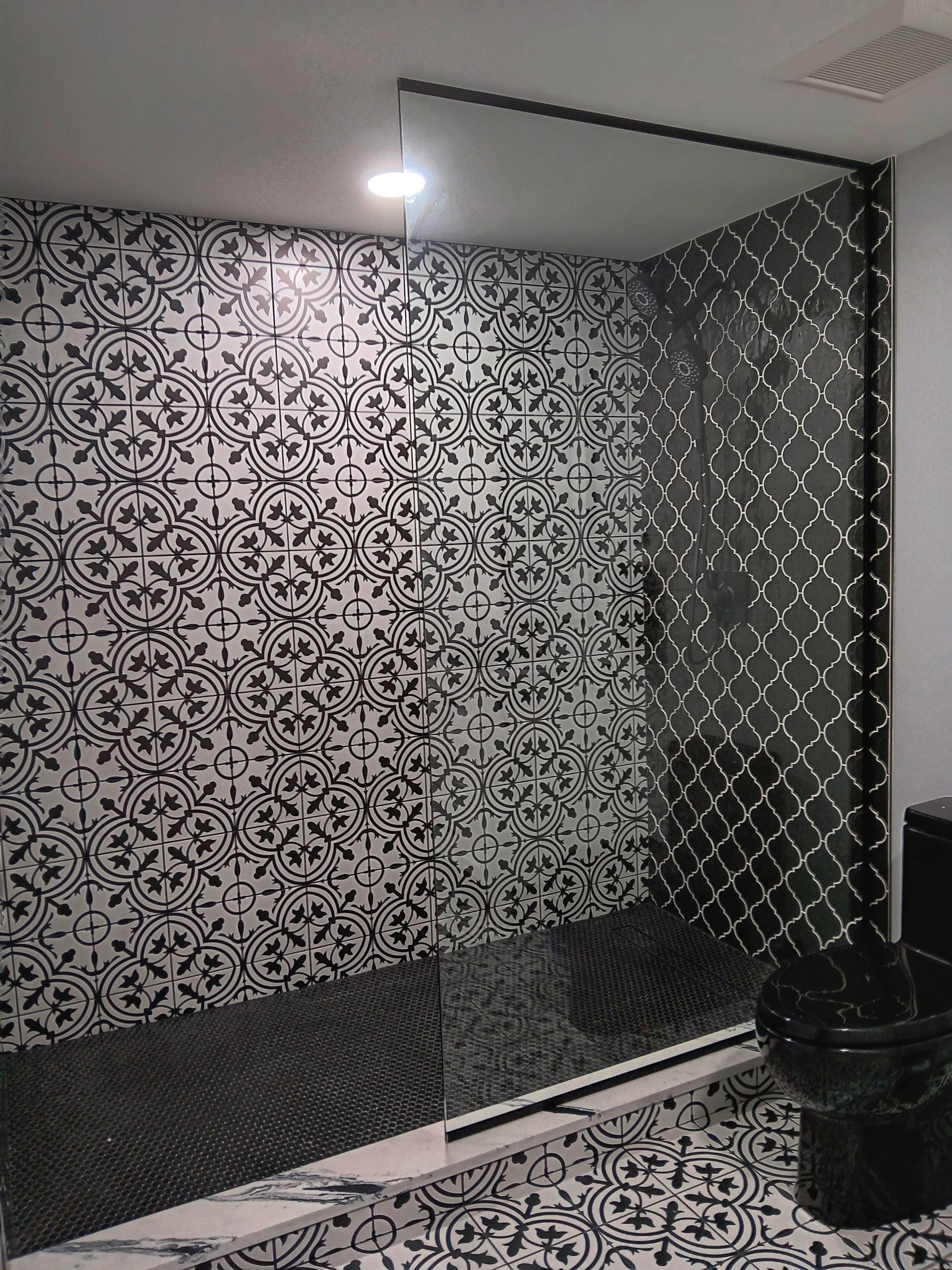 Black and white patterned tile shower with glass door.