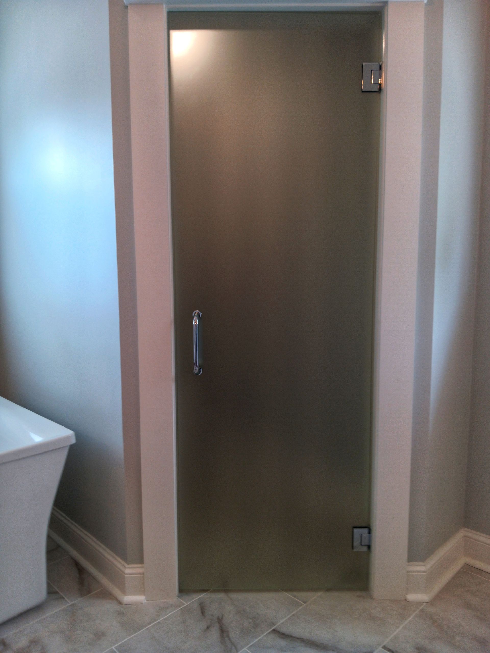 Frosted glass shower door with silver handle and hinges, in a bathroom with white trim.