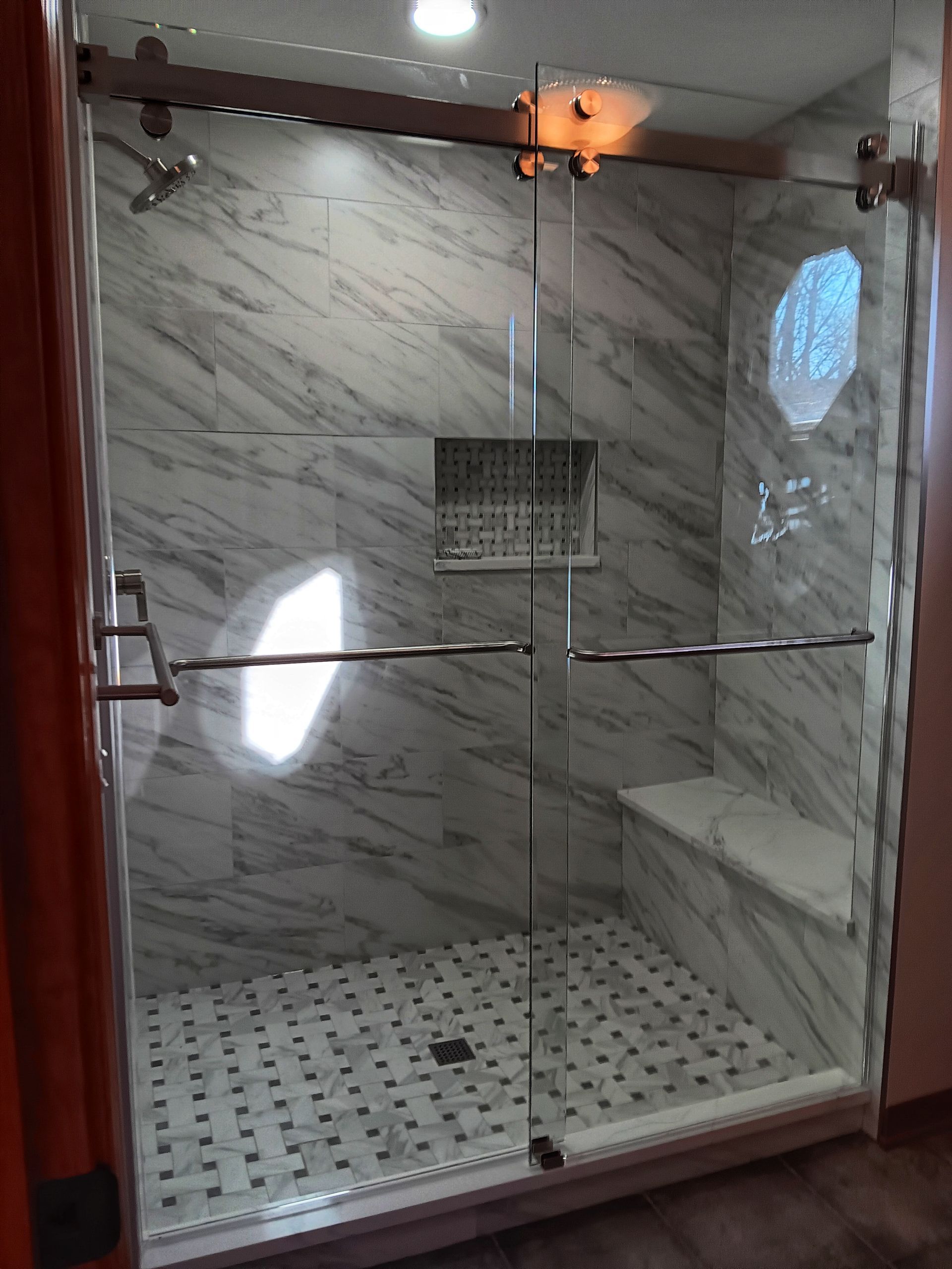 Modern glass shower with marble-look tiles, a built-in seat, and sliding door.