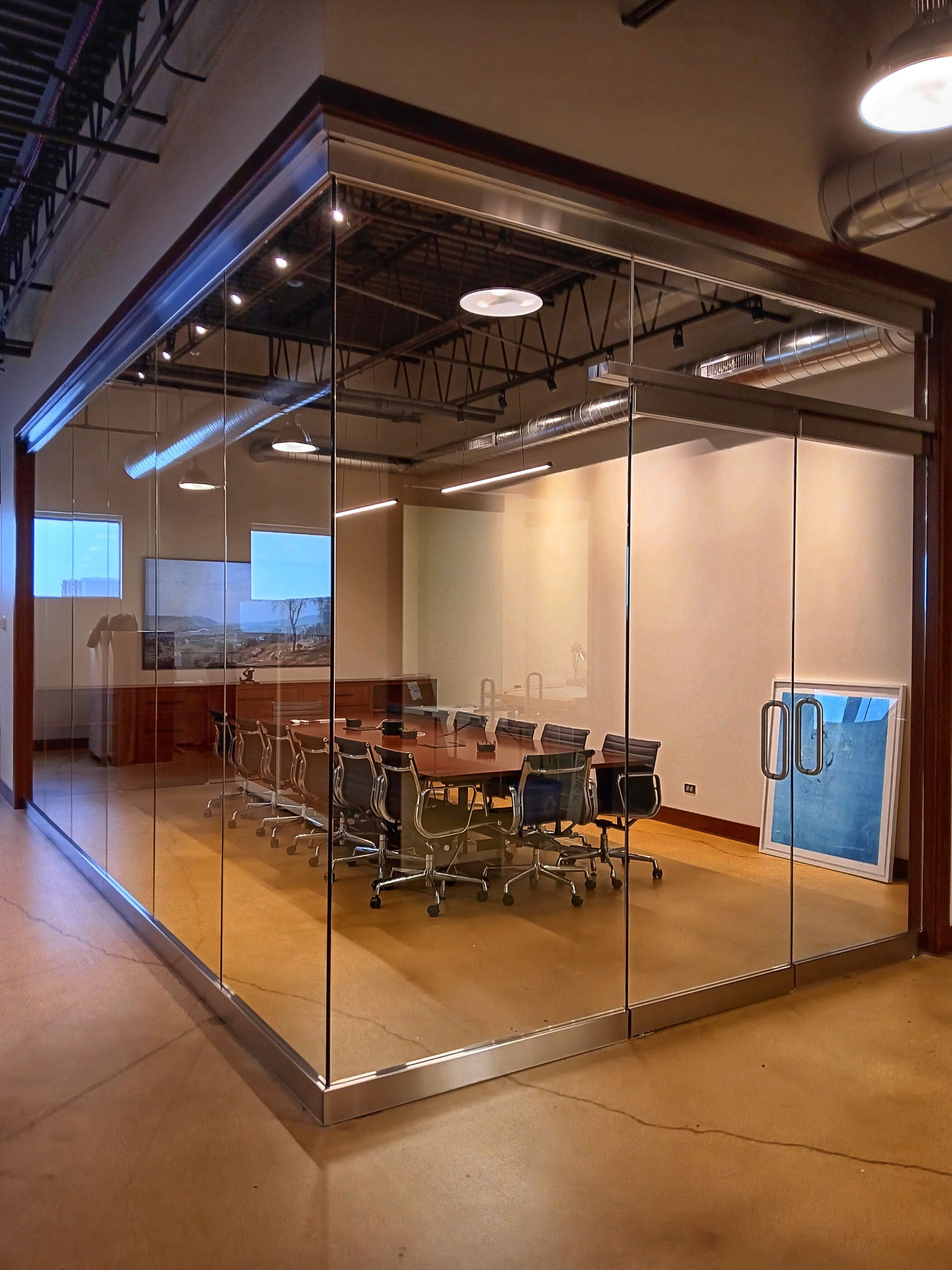 Glass-walled conference room with a wooden table, chairs, and a cityscape view.