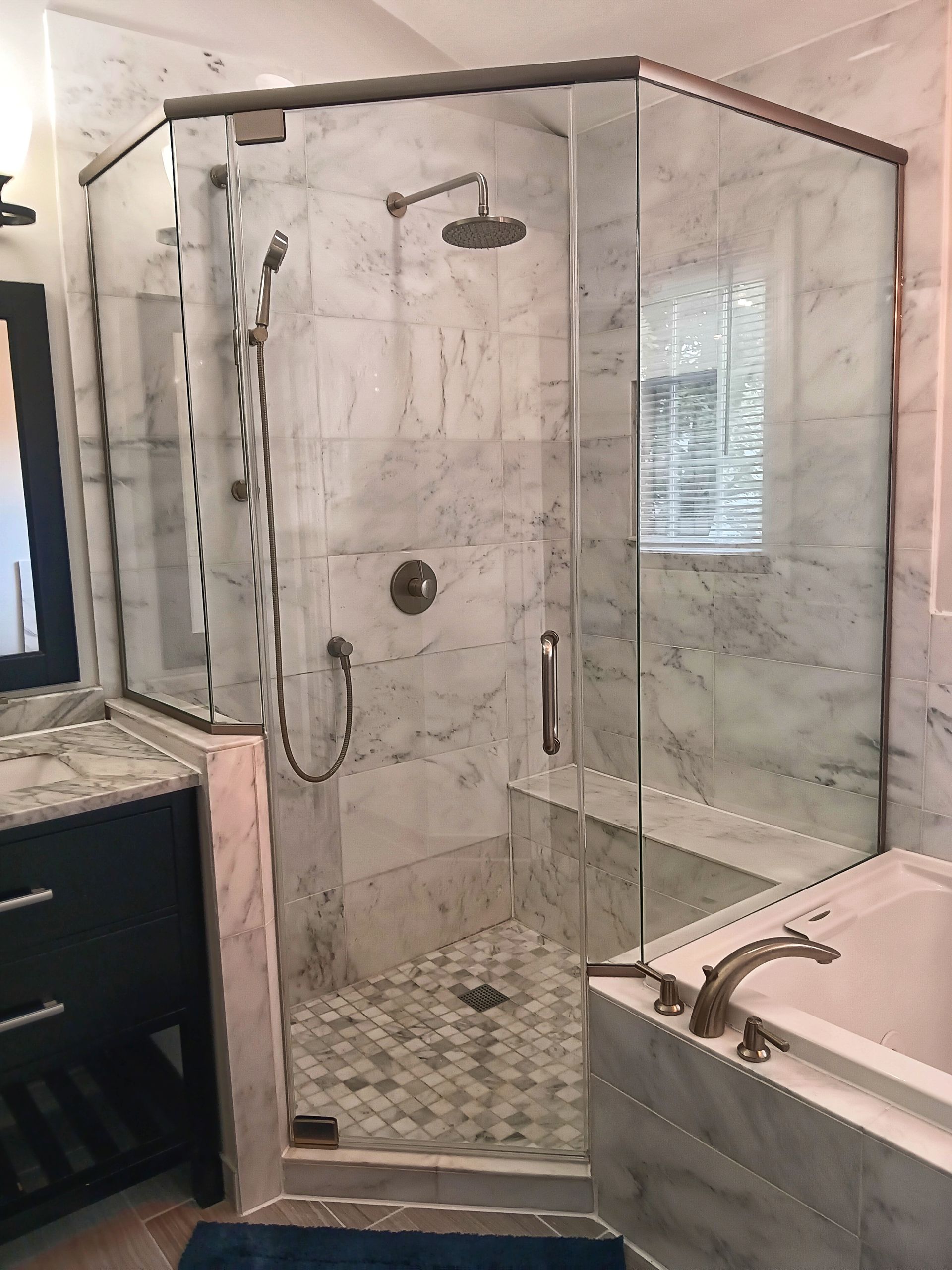 Marble shower with glass doors and bronze fixtures in a bathroom.