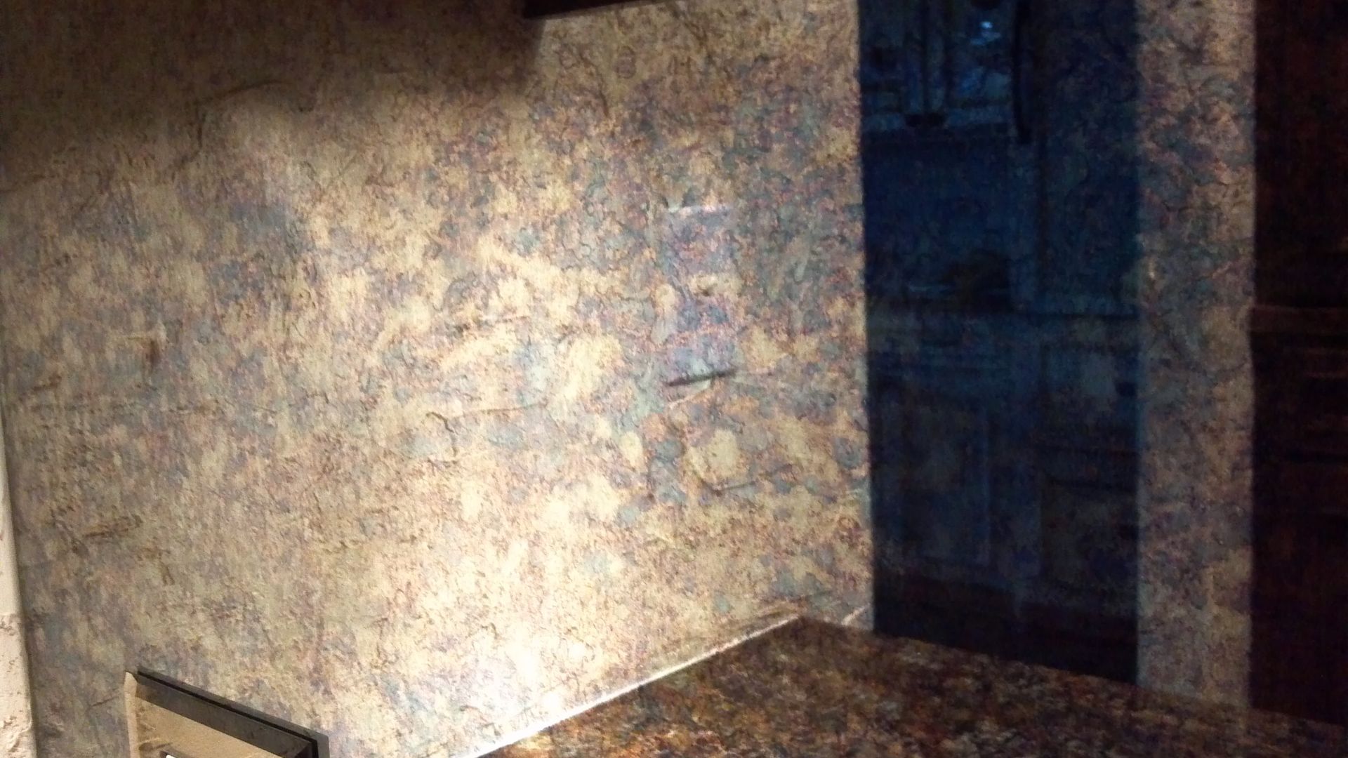 Textured wall with electrical outlet. Dark granite countertop in a dimly lit room.