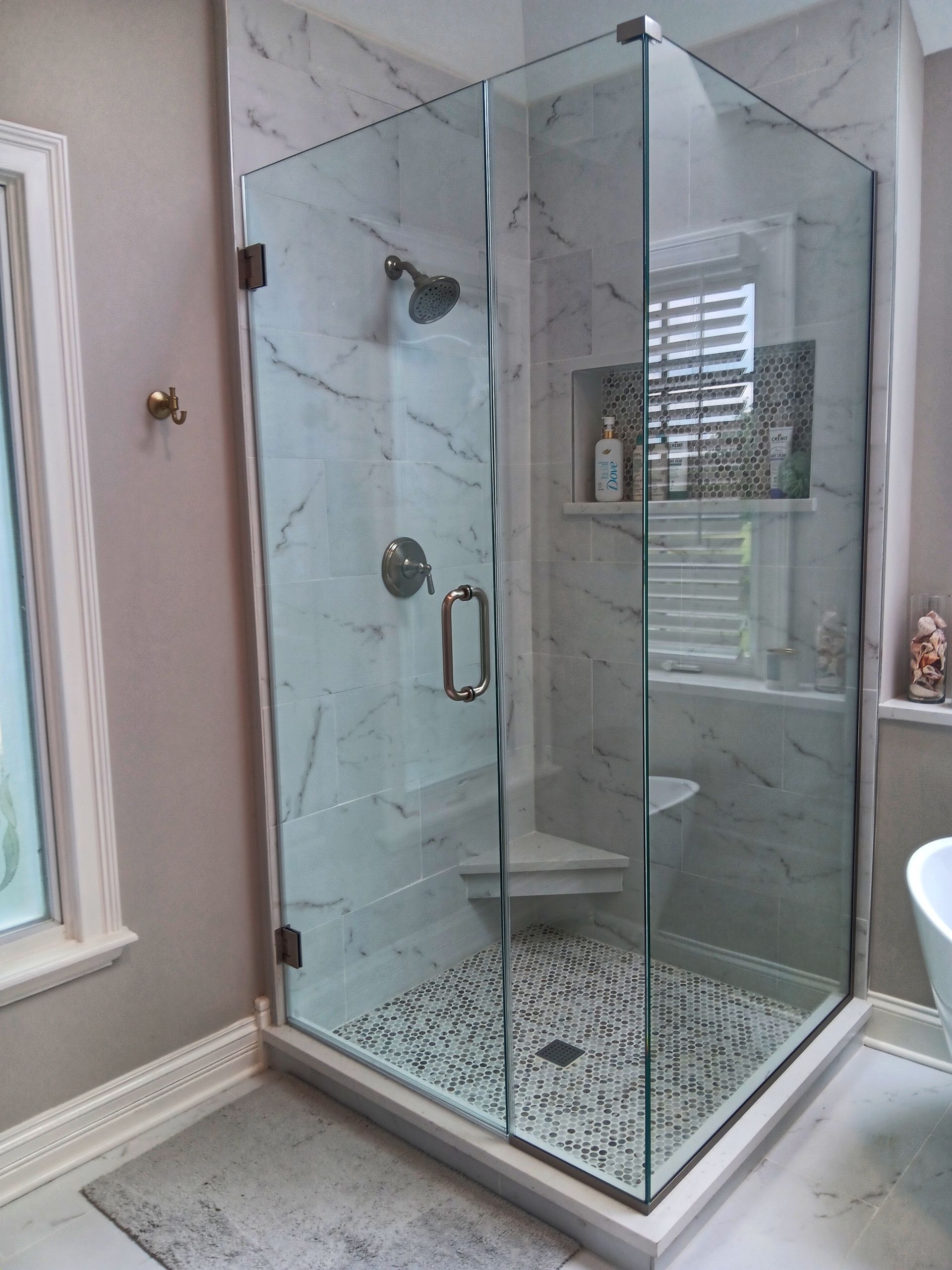 Glass corner shower with marble tile, pebble floor, and built-in shelf.