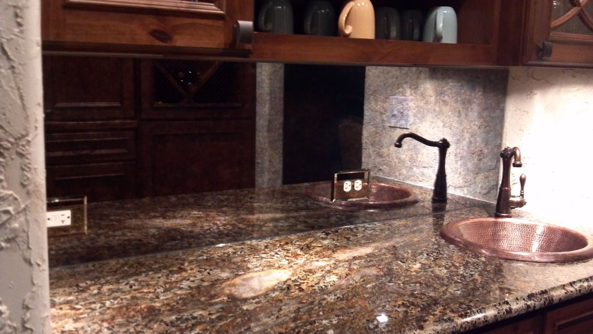 Granite countertop with copper sink, faucet, and mirrored backsplash in a kitchen.