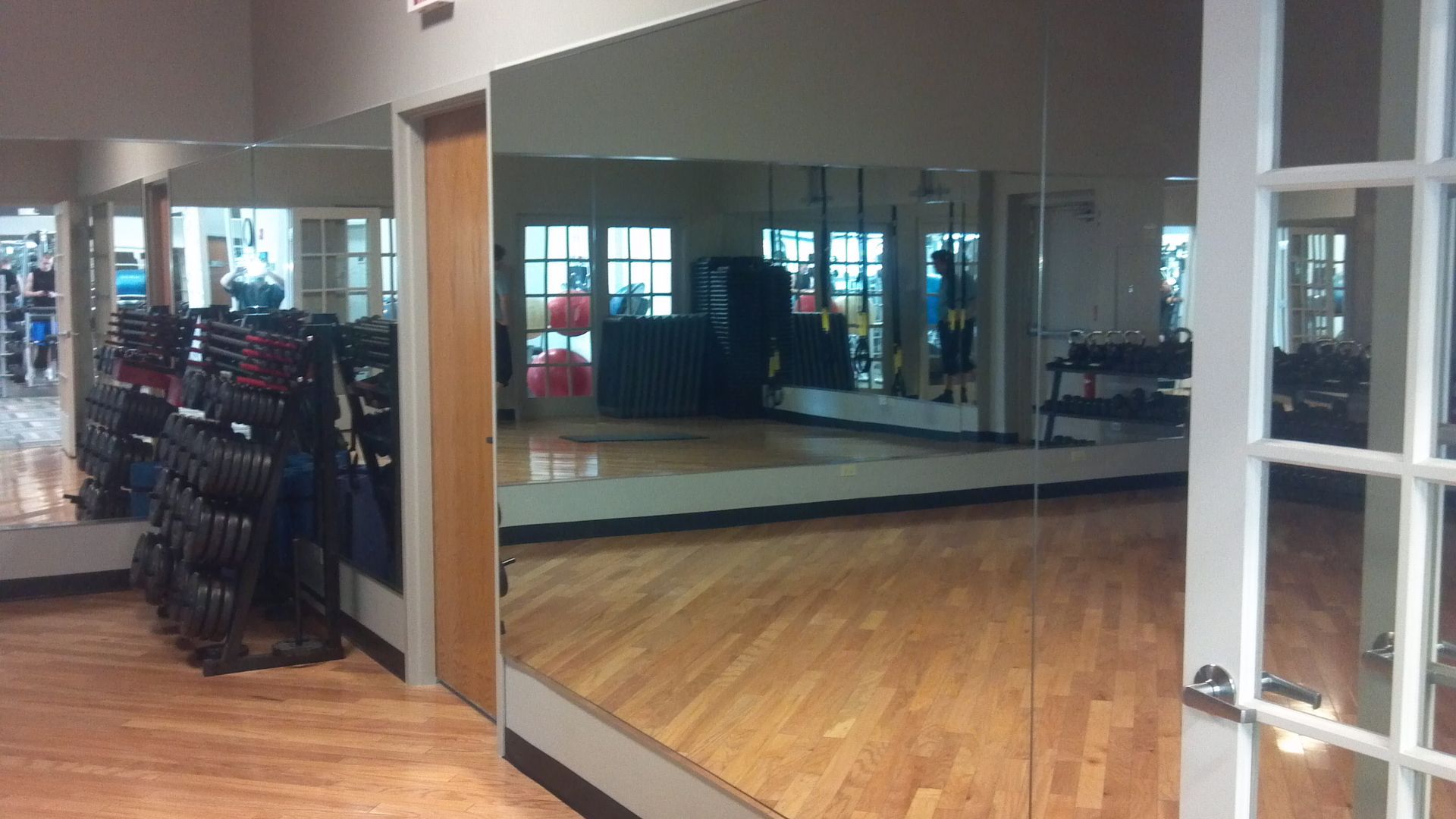 Gym interior with mirrors on the walls, weights, and hardwood floor.