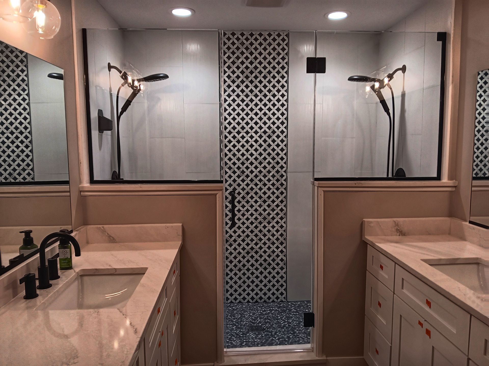 Bathroom with white double vanity and shower with patterned tile wall.