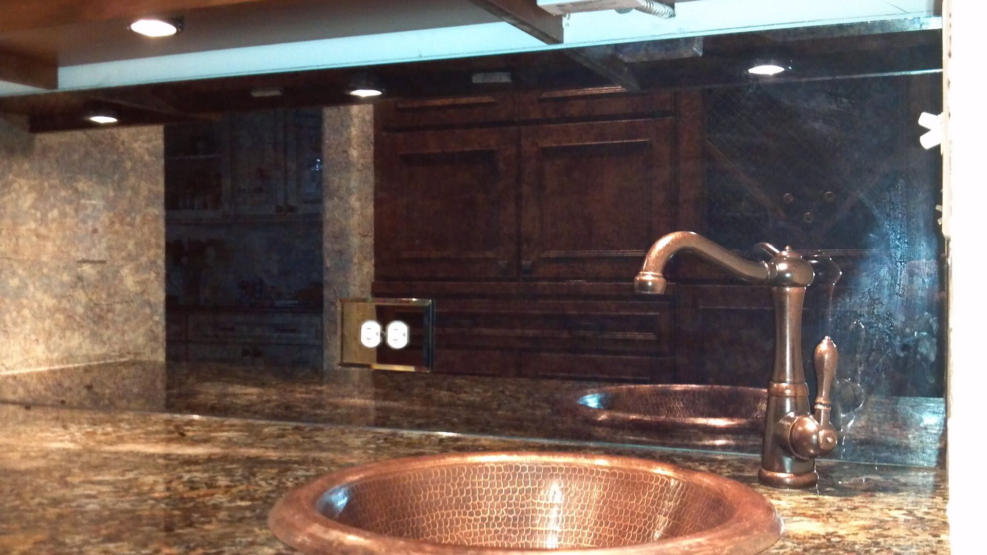 Copper sink and faucet in a kitchen with dark cabinets and granite countertops.