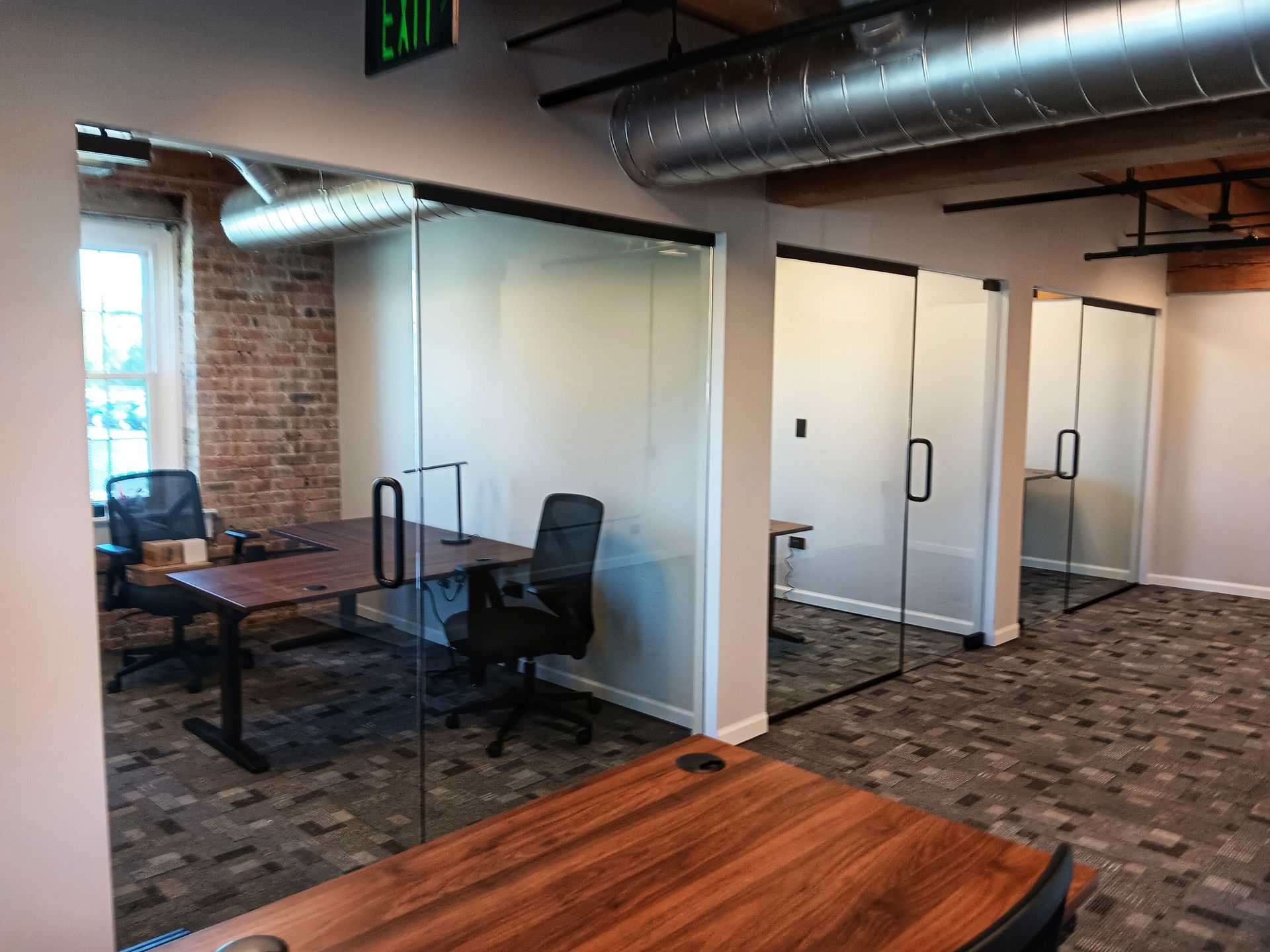 Office space with glass-walled cubicles, exposed brick, and industrial ceiling.
