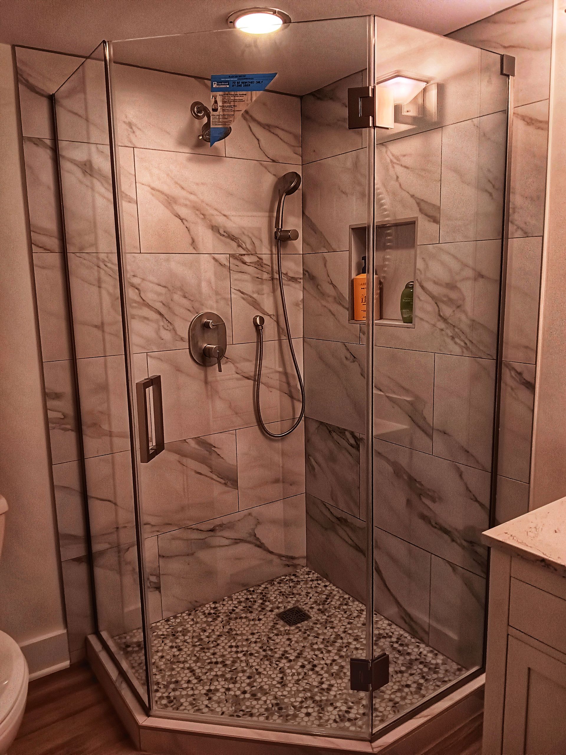 Glass-enclosed shower with marble tile walls, pebble floor, and chrome fixtures.