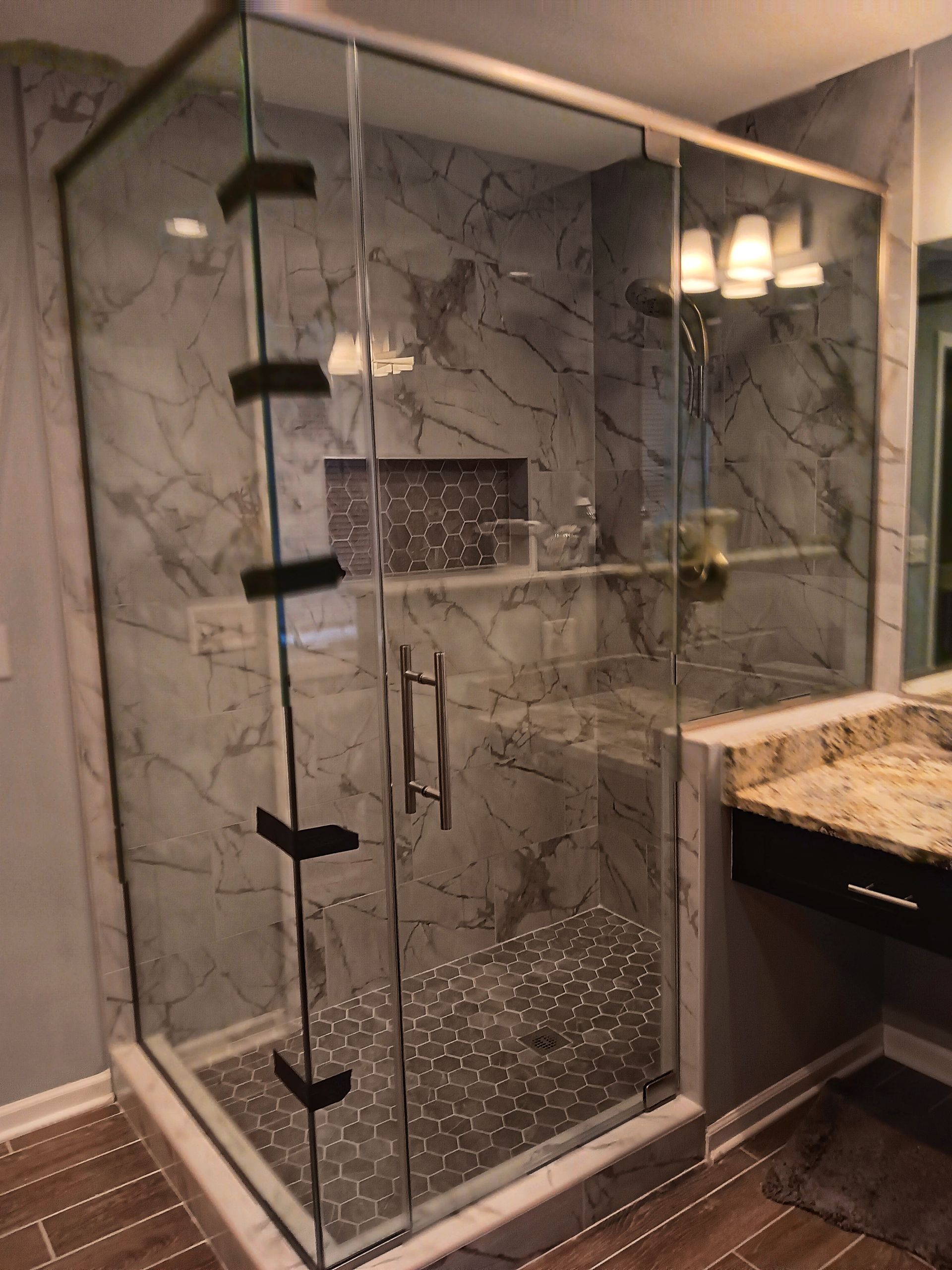 Glass shower enclosure with gray marble tile, black accents, and a marble countertop.