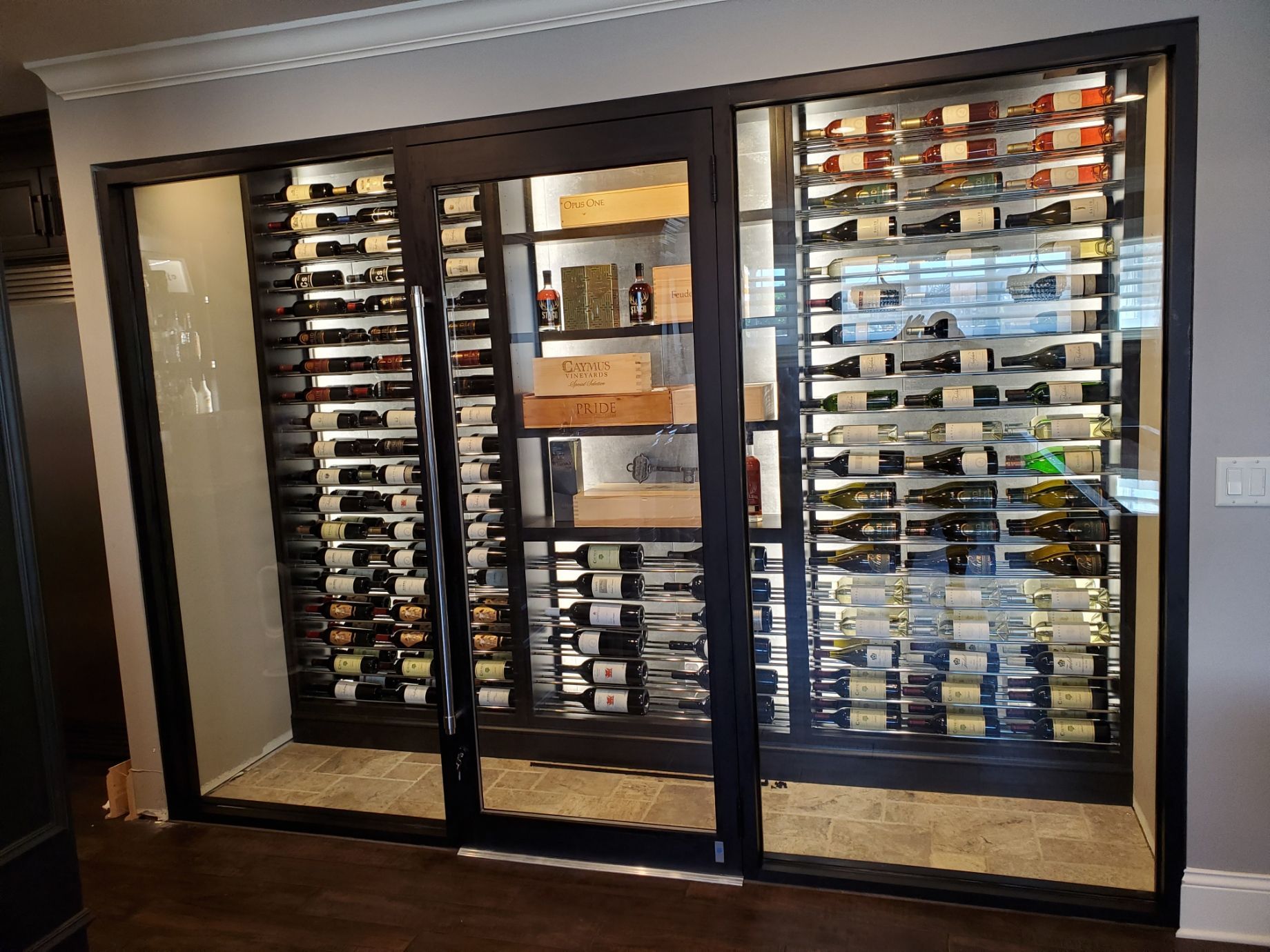 Wine cellar with glass doors, backlit bottles displayed on racks, dark frame.