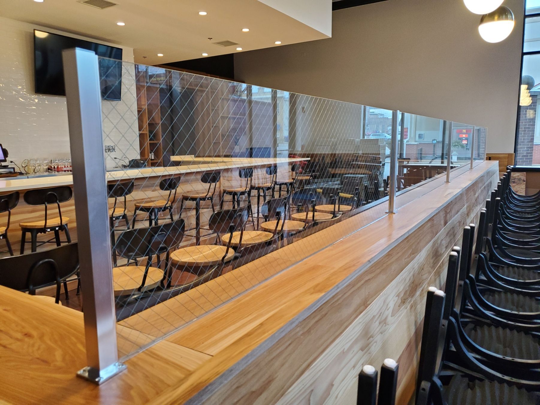 Clear plexiglass dividers separate seating areas in a restaurant, with empty tables and chairs visible.