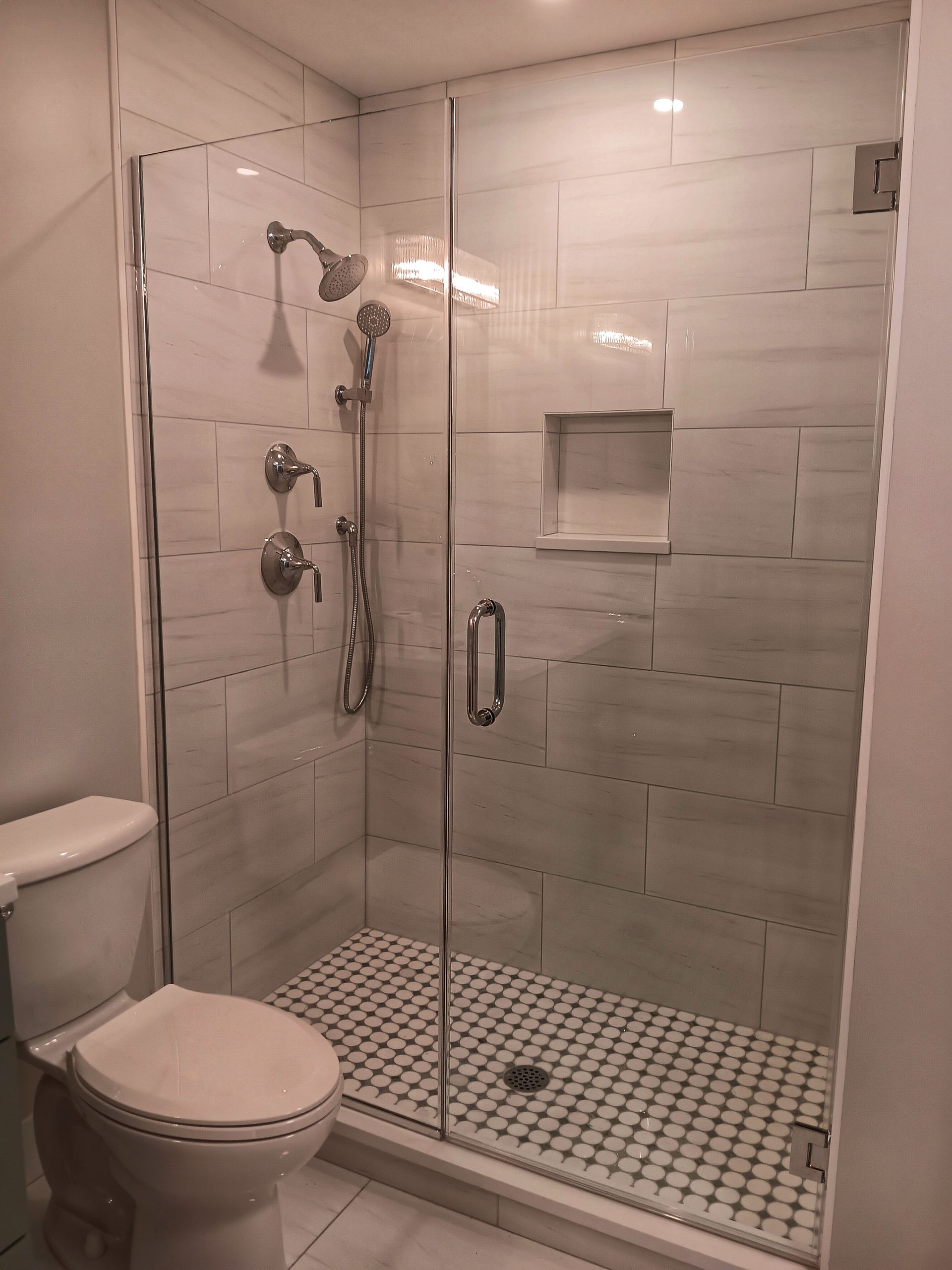 Modern bathroom with glass shower, white tile walls, and a small toilet.
