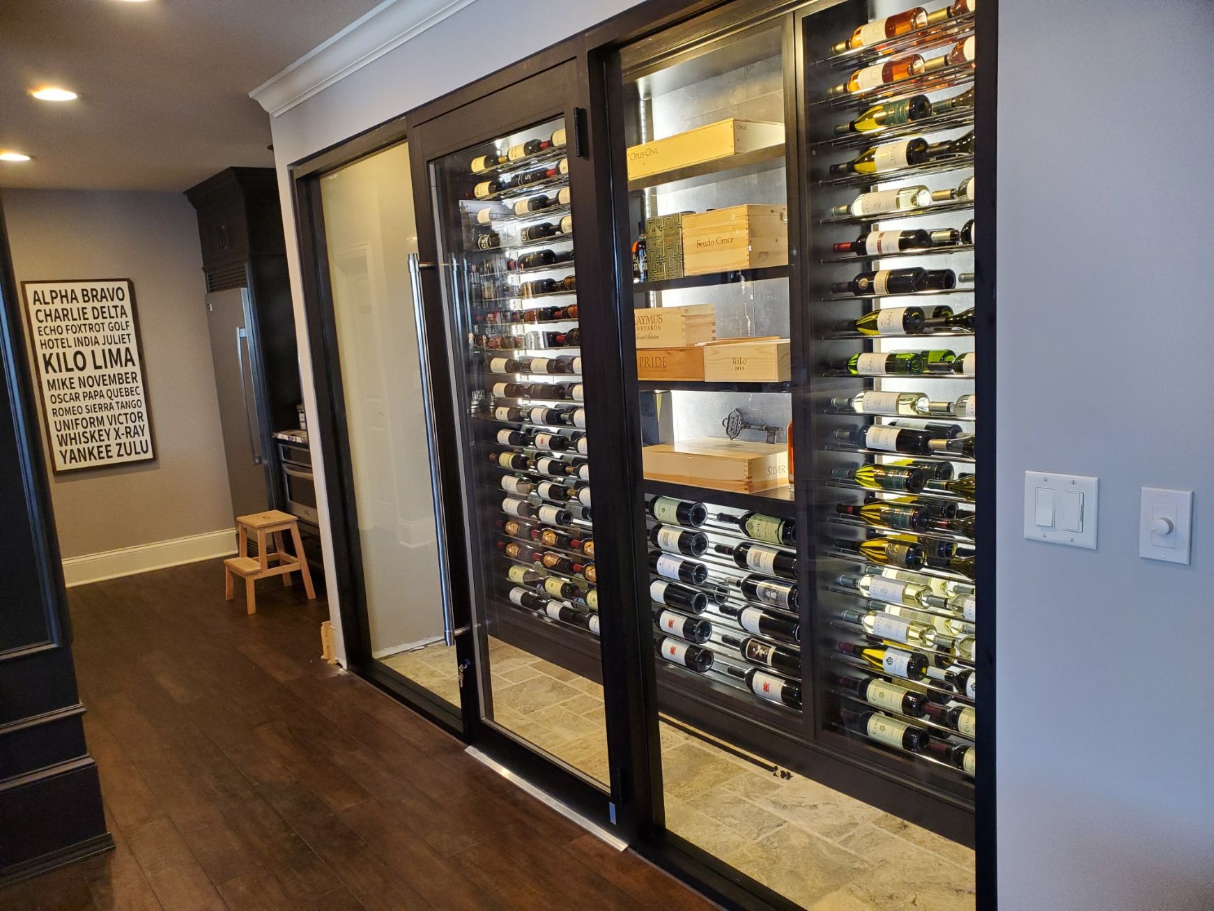 Wine cellar with sliding glass doors; bottles on display with wooden boxes; dark trim.
