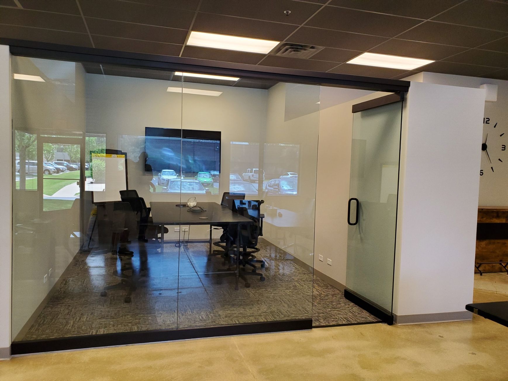 Glass-walled conference room with table, chairs, TV, and exterior view; polished concrete floor.