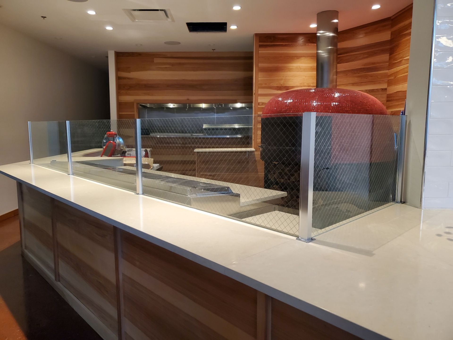 Restaurant kitchen with a wood-fired pizza oven, counter, and protective glass, in a light, modern space.