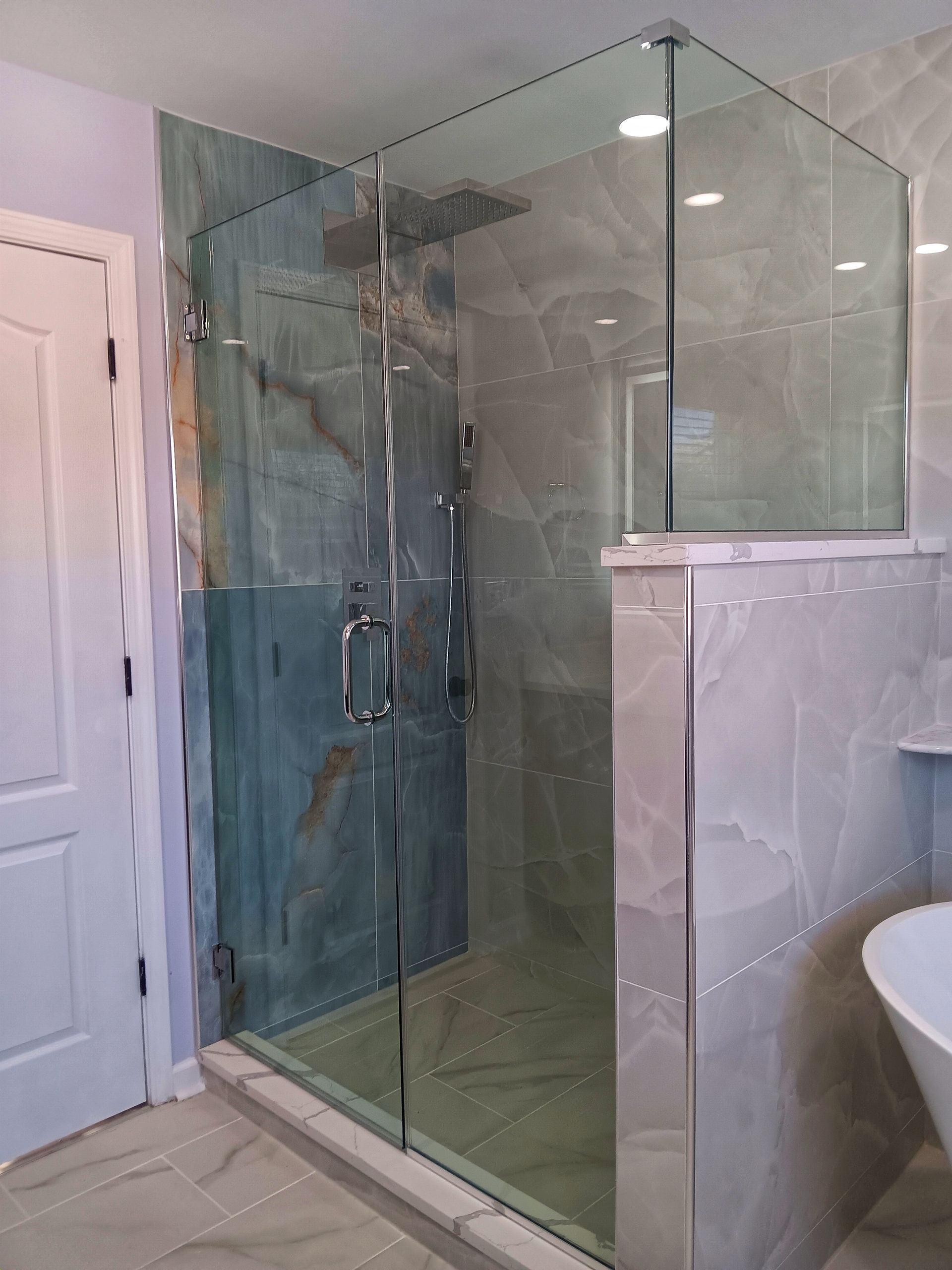 Glass shower enclosure with gray tile and green-blue wall; chrome fixtures and door handle.