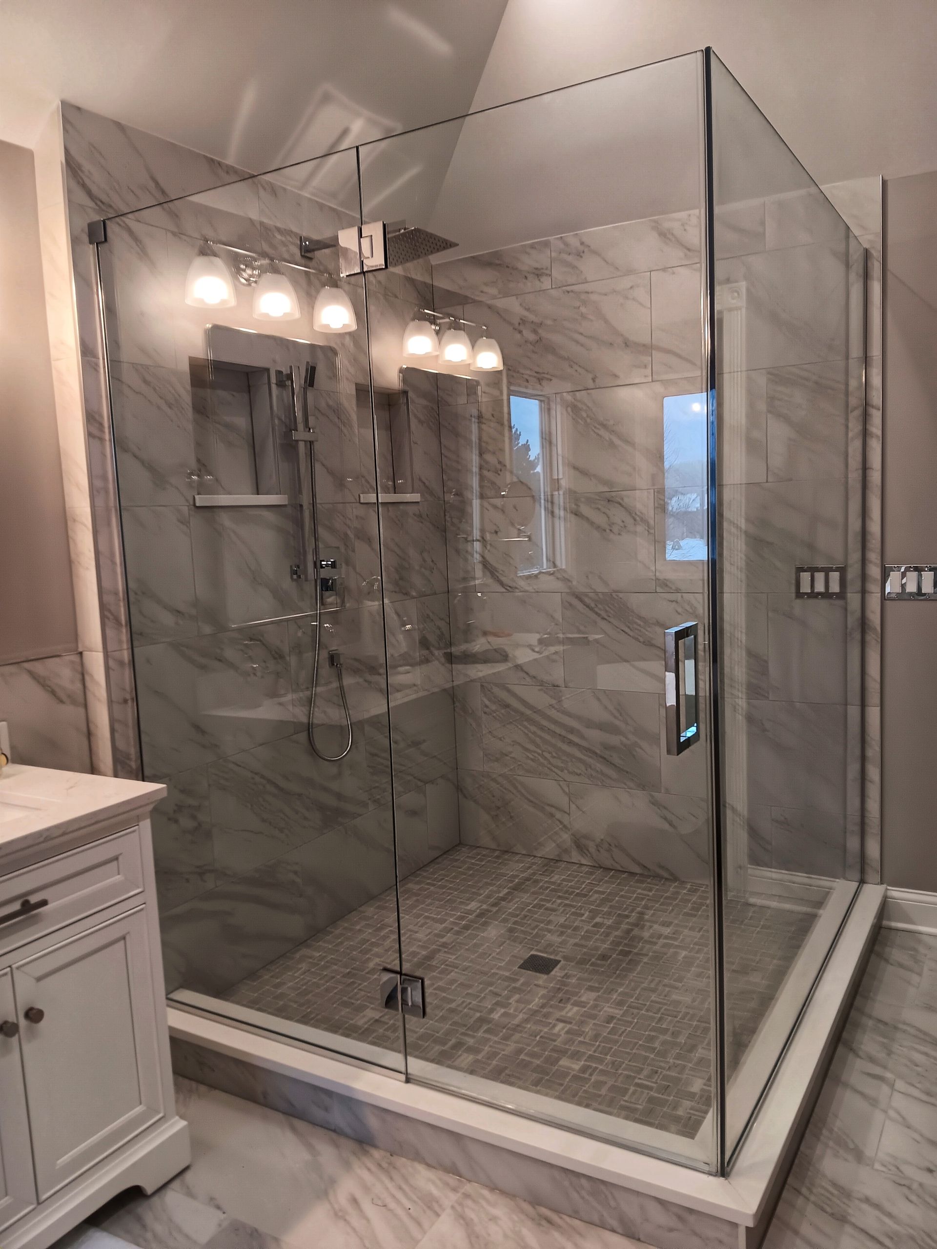 Glass shower enclosure with gray marble tile, chrome fixtures, and a white vanity.