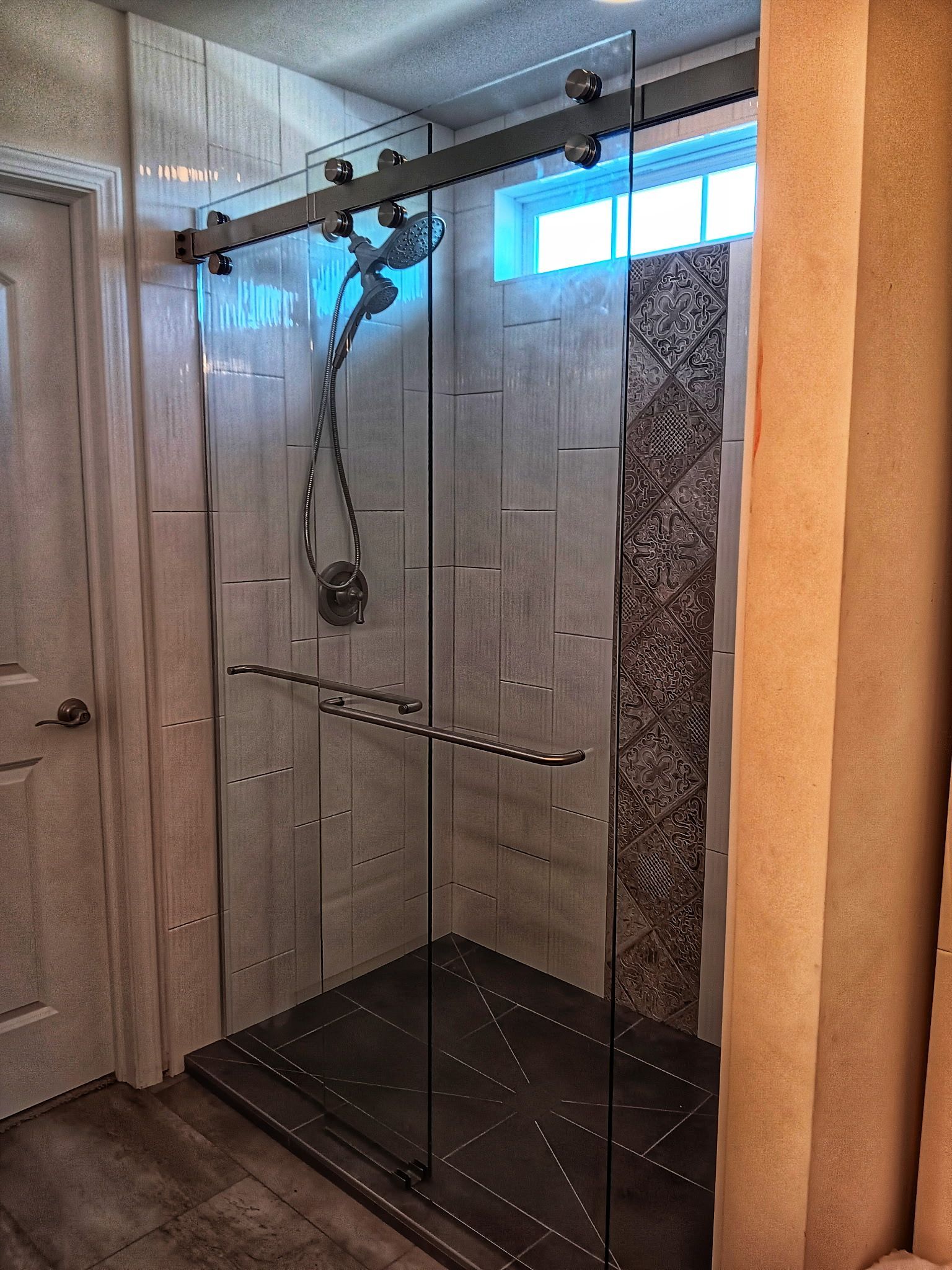 Modern shower with glass doors, stone accent wall, and sliding hardware.