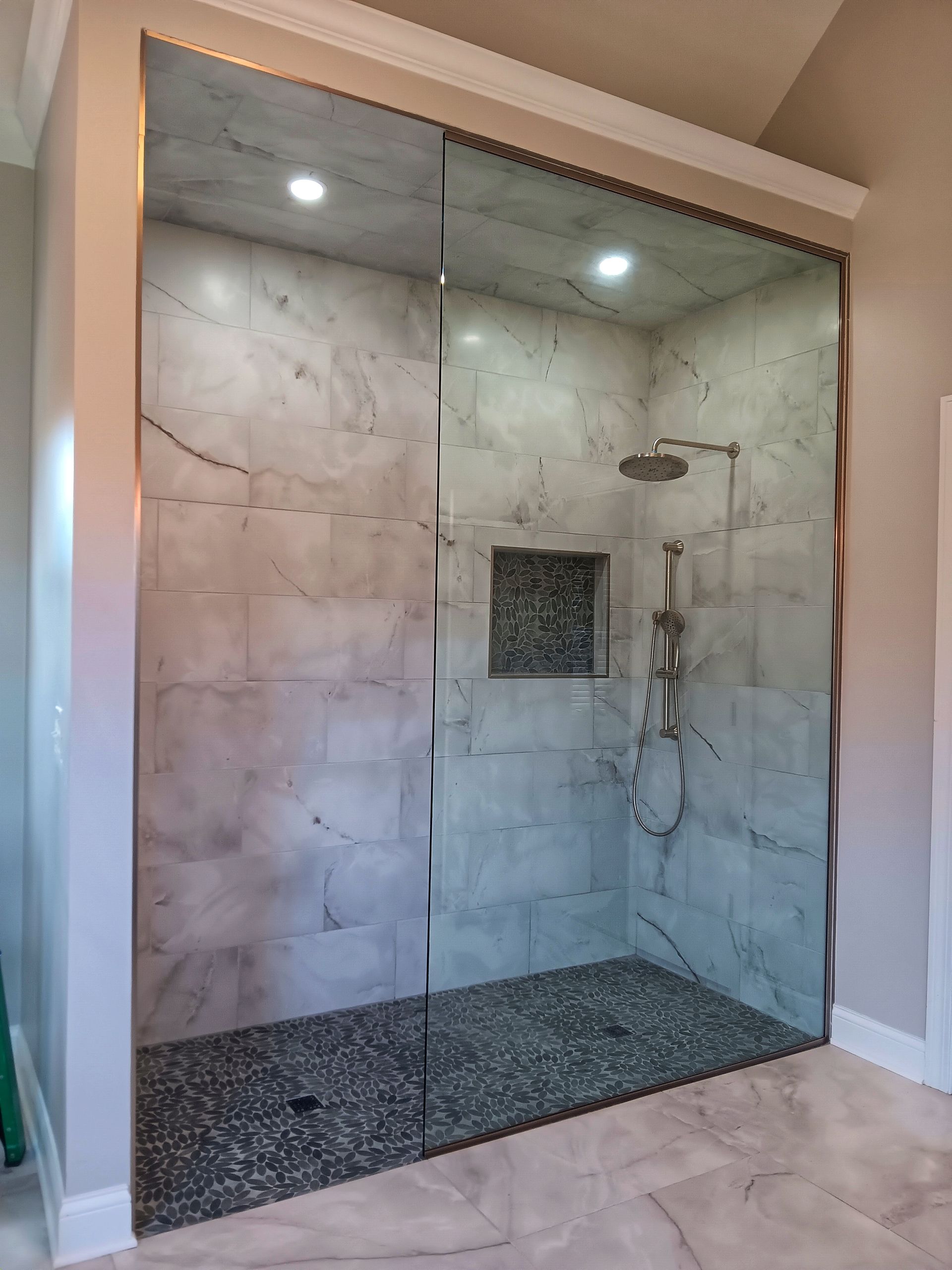 A modern shower with marble tile walls, a pebble floor, glass enclosure, and a recessed soap niche.