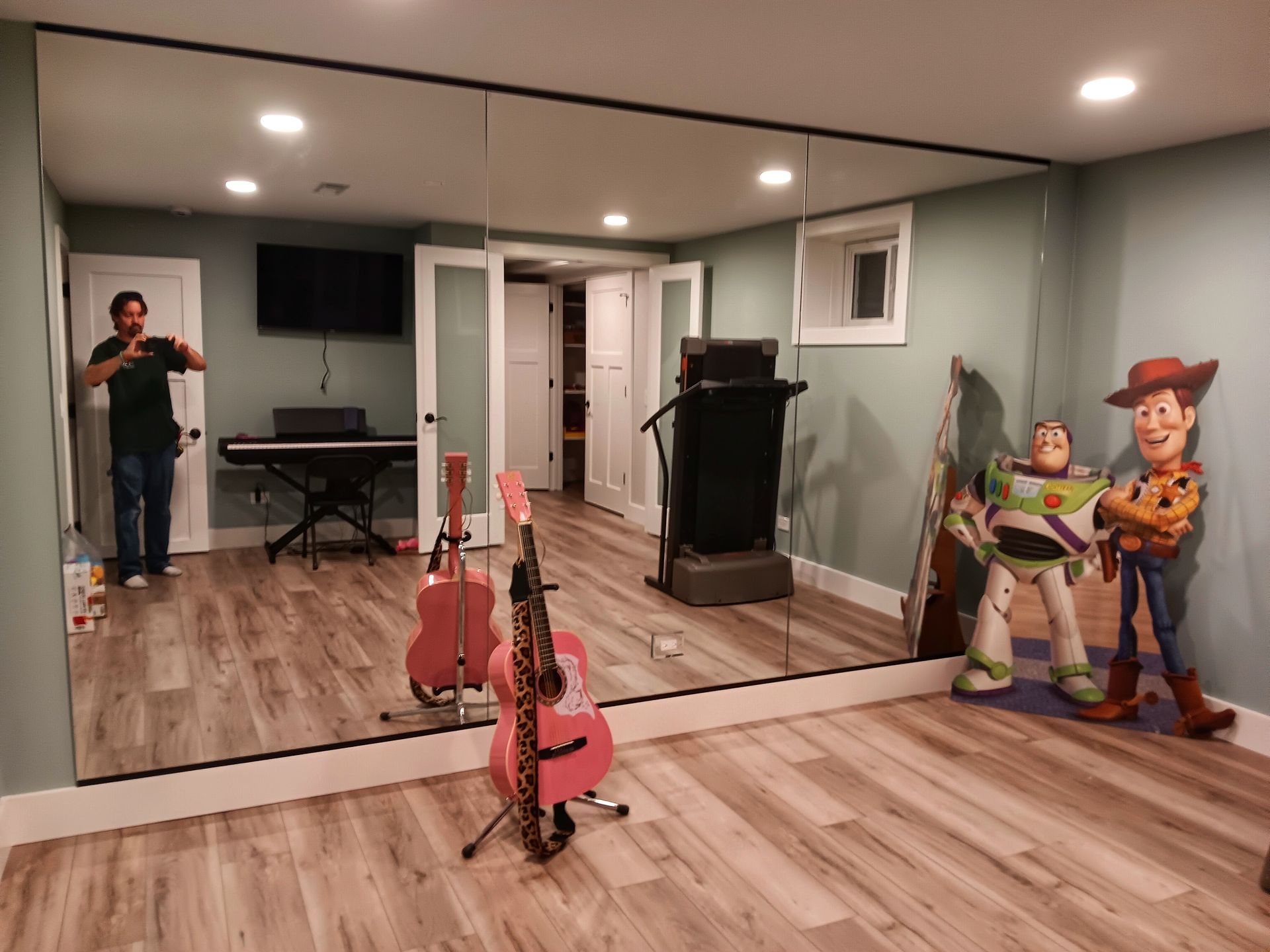 Man in room with mirrors, guitars, toy story characters, and workout equipment.