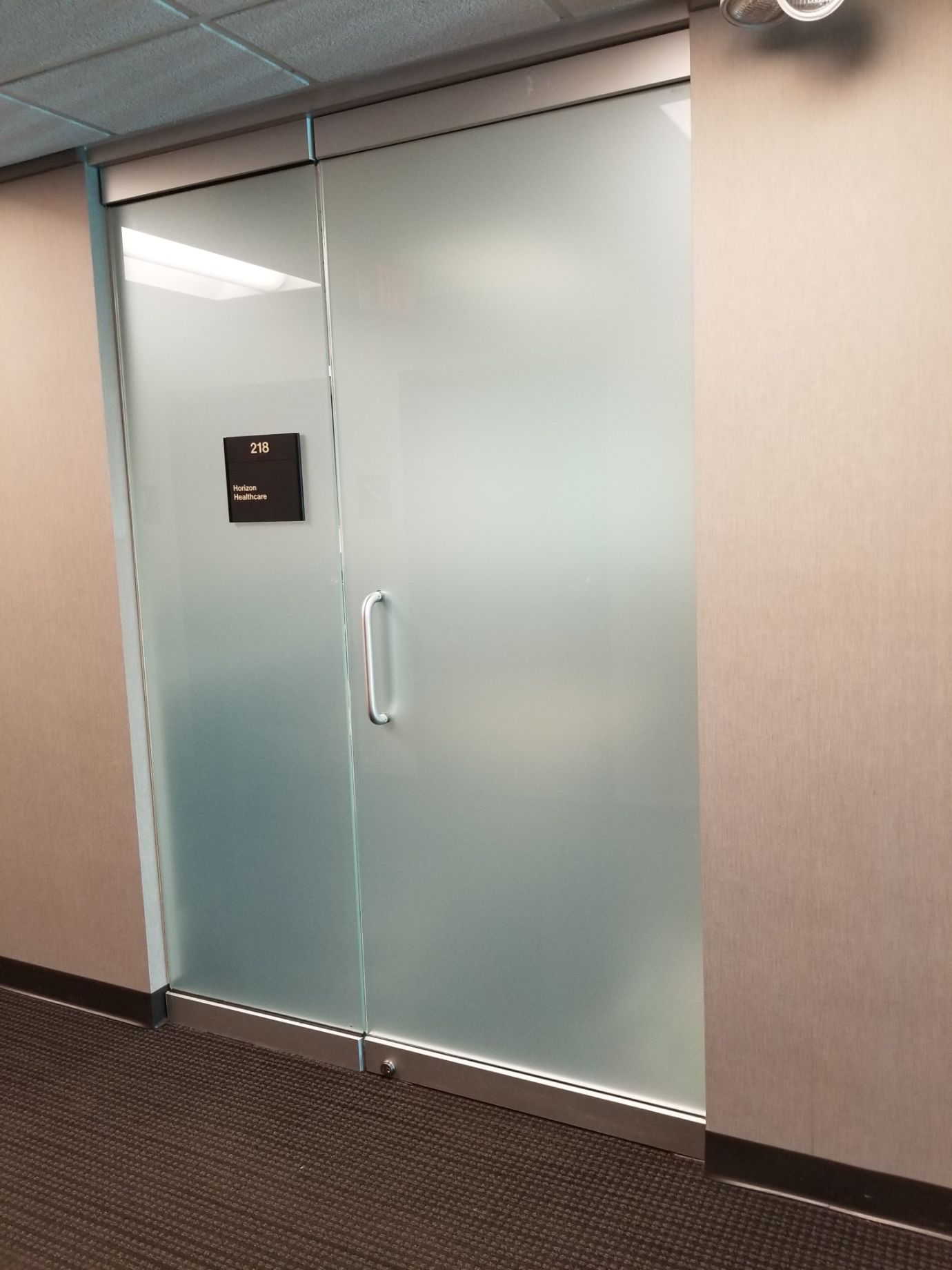 Frosted glass door with a silver handle and a black sign in a hallway.