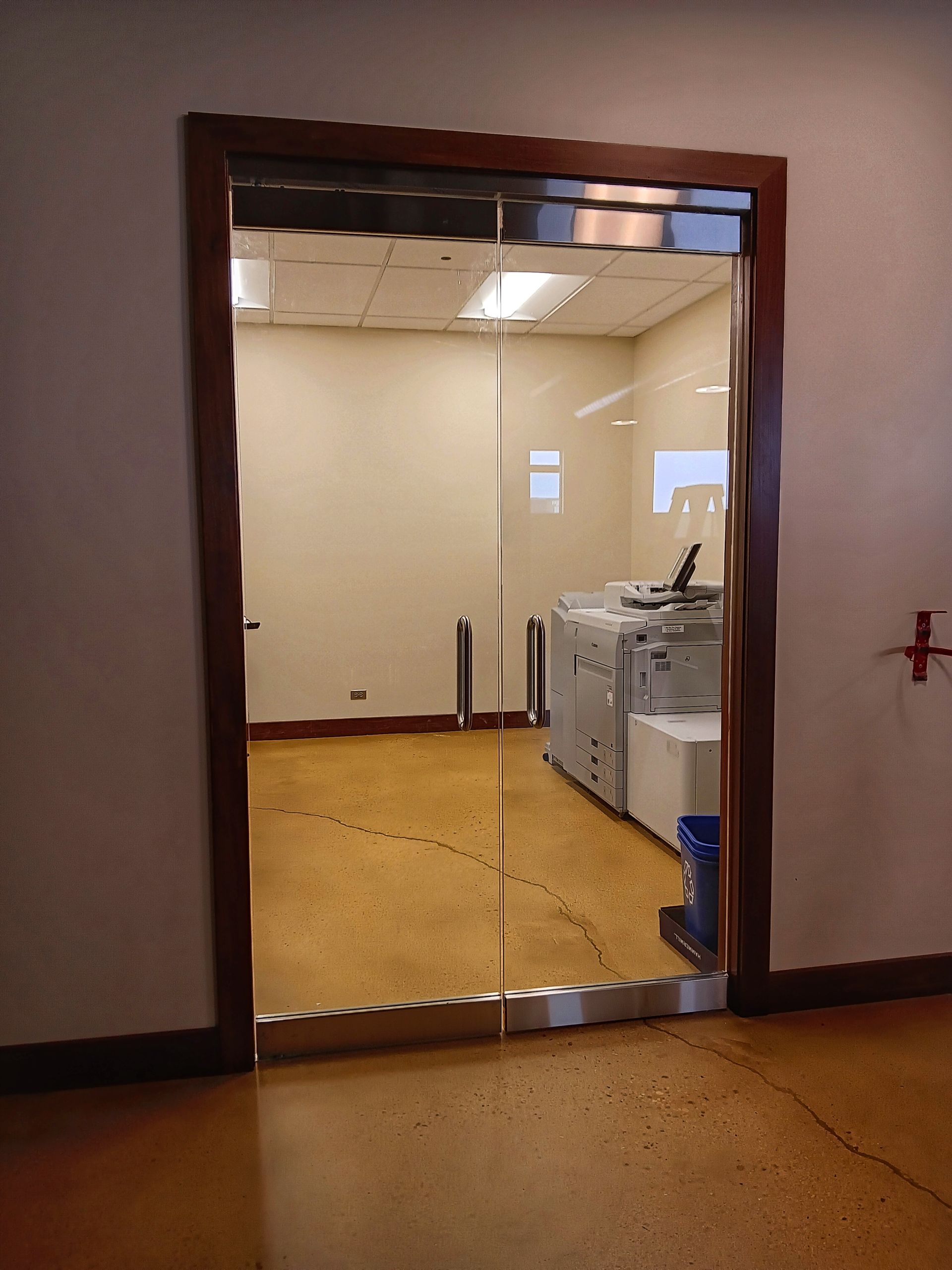 Glass door leading to a room with a copier and tan walls.