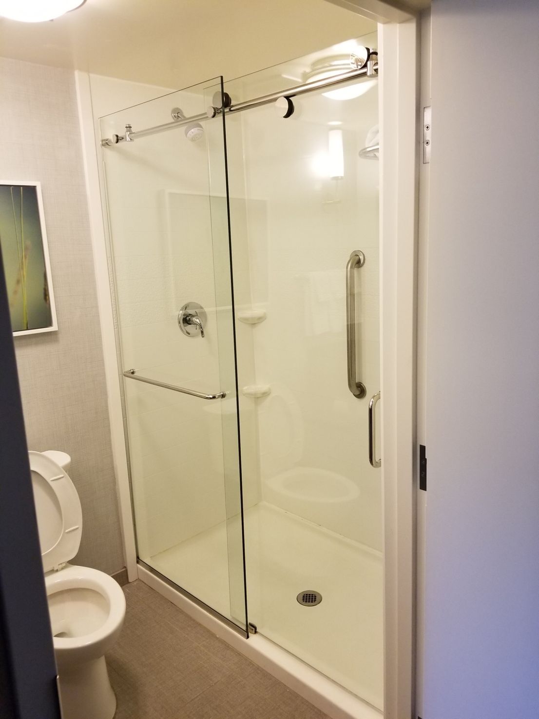 Bathroom with white shower stall, sliding glass doors, and grab bar. Toilet to the left.