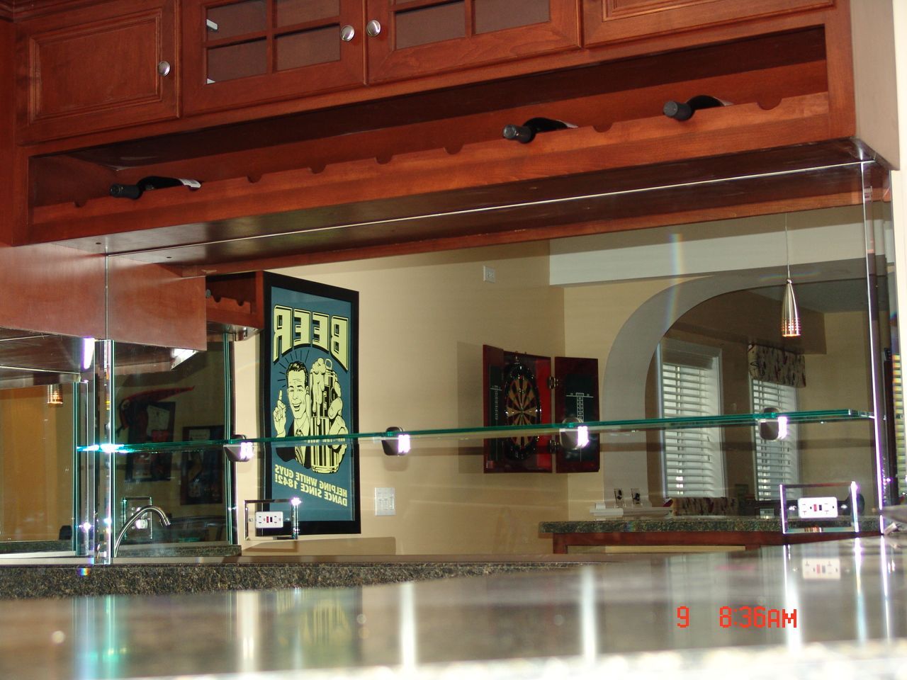 A home bar with a glass divider, wooden cabinets, and beer sign.