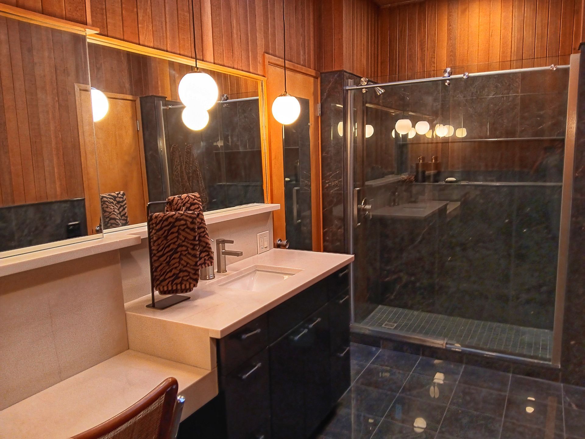 Bathroom with dark marble shower, vanity with wood paneling, and globe lights.