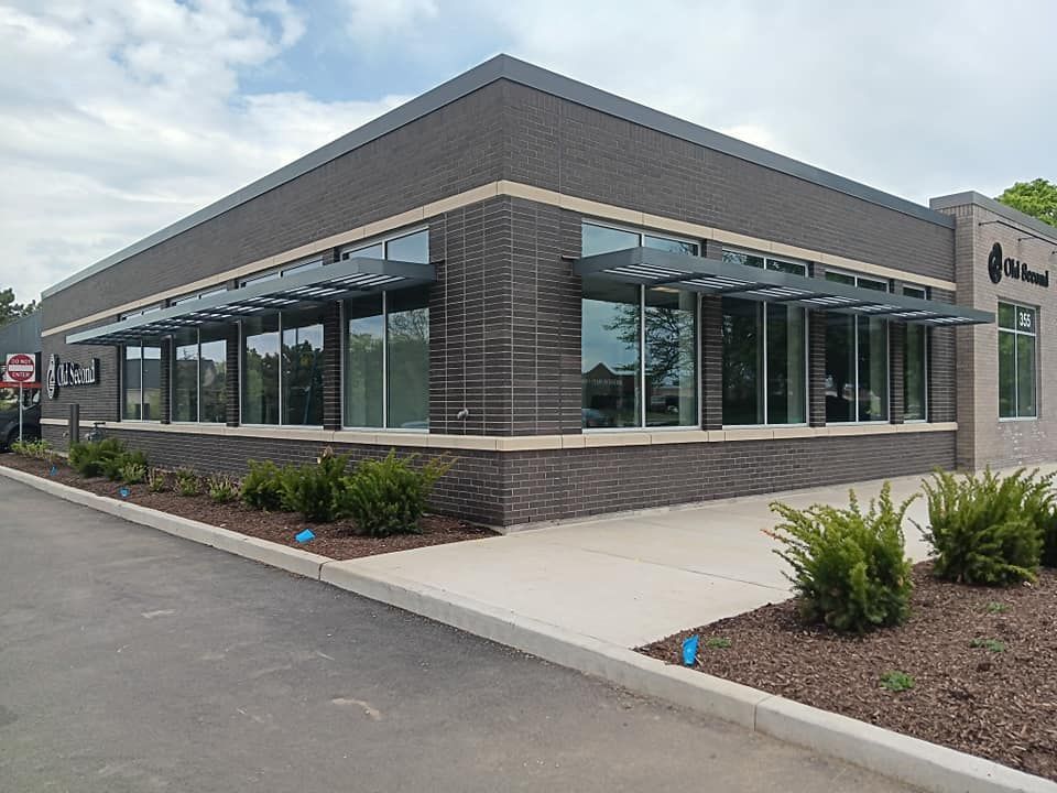 Modern brick building with large windows and metal awnings; landscaping in front.