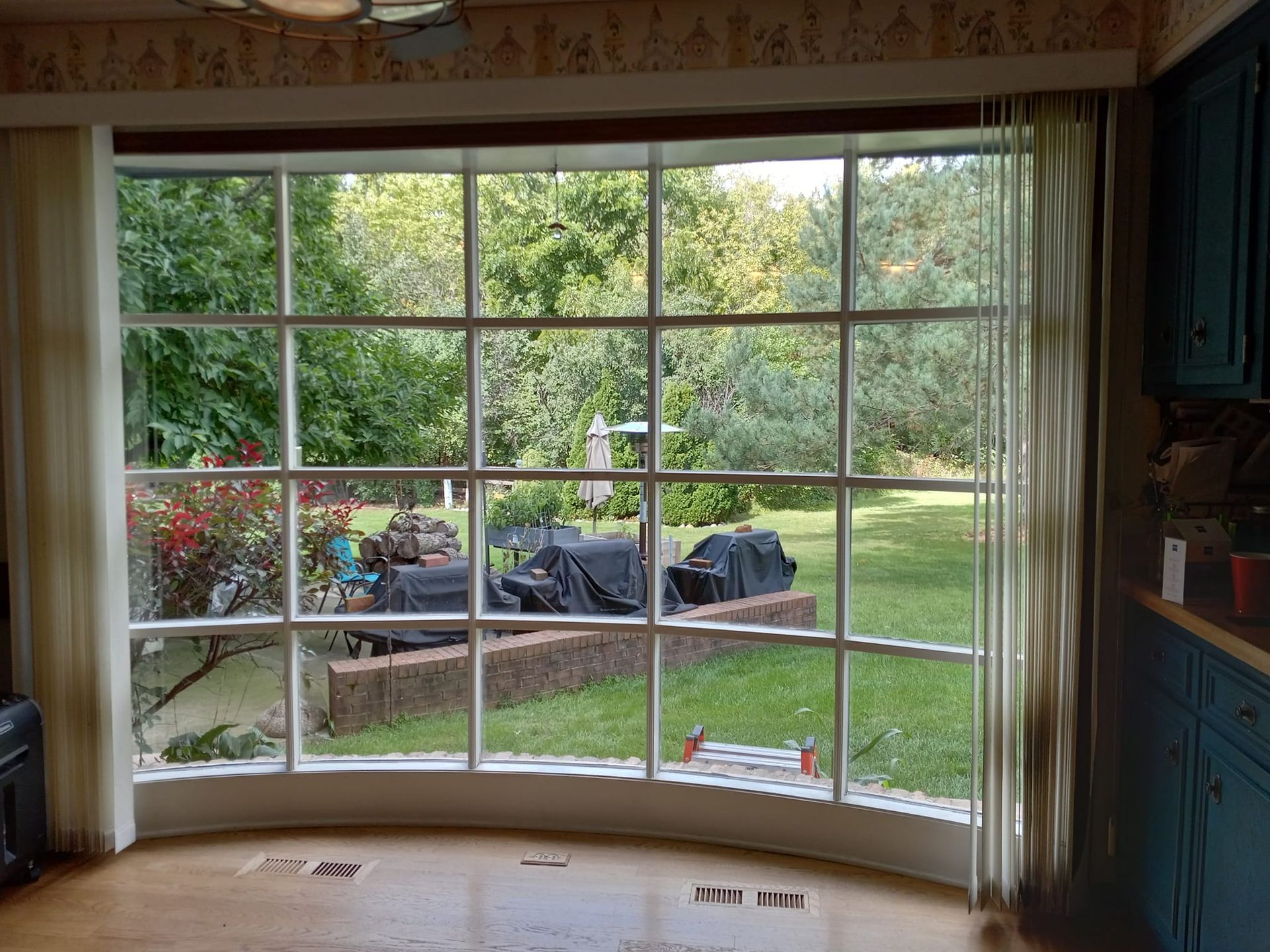 A large, curved window with a grid pattern, looking out onto a backyard. Curtains on either side.