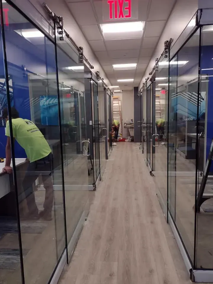 Hallway with glass-walled offices. A person leans on a desk. Red 