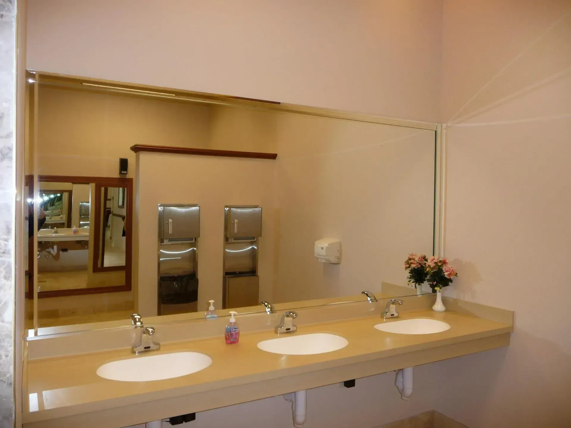 Public restroom with three sinks, large mirror, and paper towel dispensers.