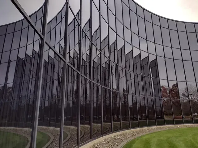 Curved modern building with reflective glass facade, reflecting overcast sky and green lawn.